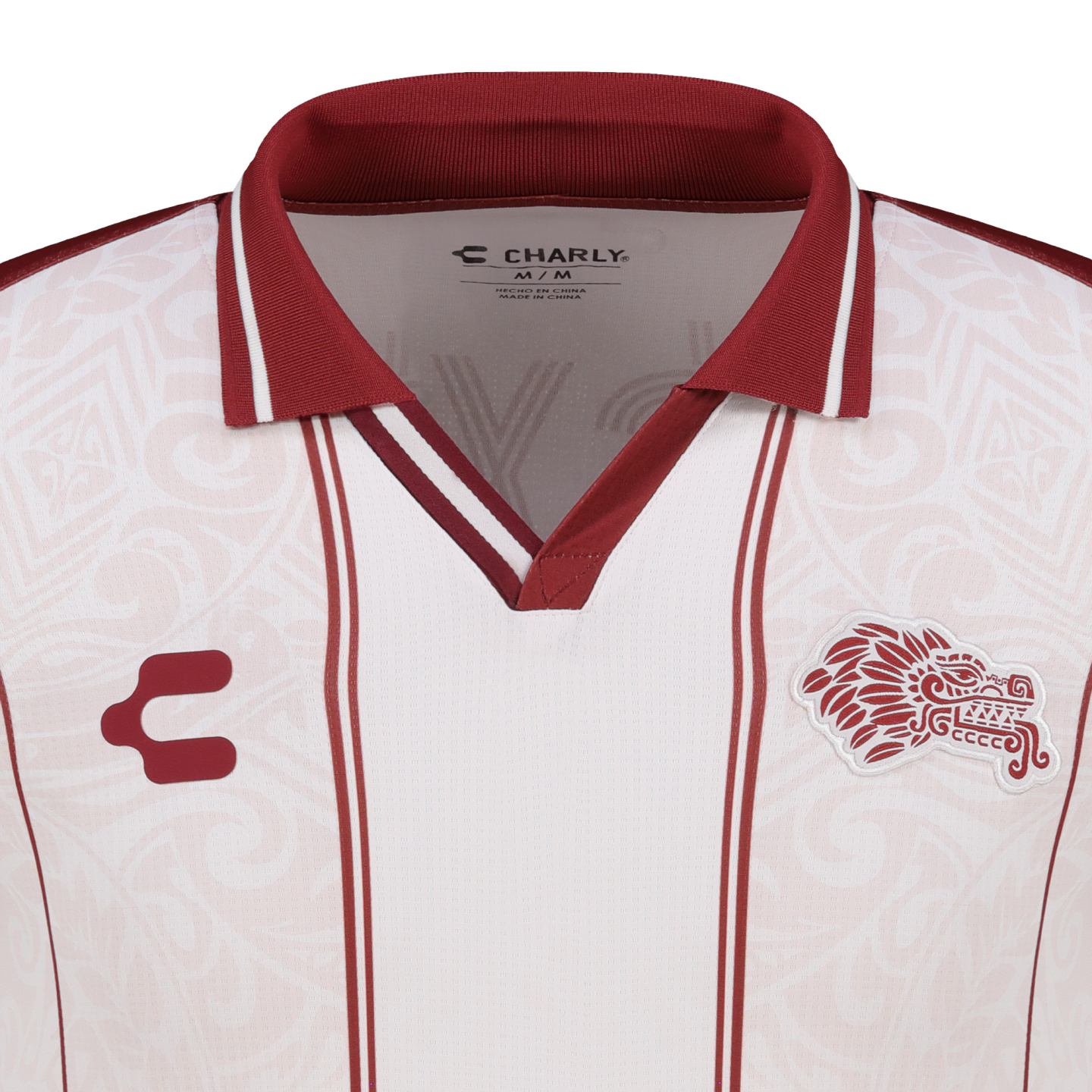 White soccer jersey by Charly with a maroon collar and stripes. It features an Aztec-style feathered serpent crest and tonal patterns.