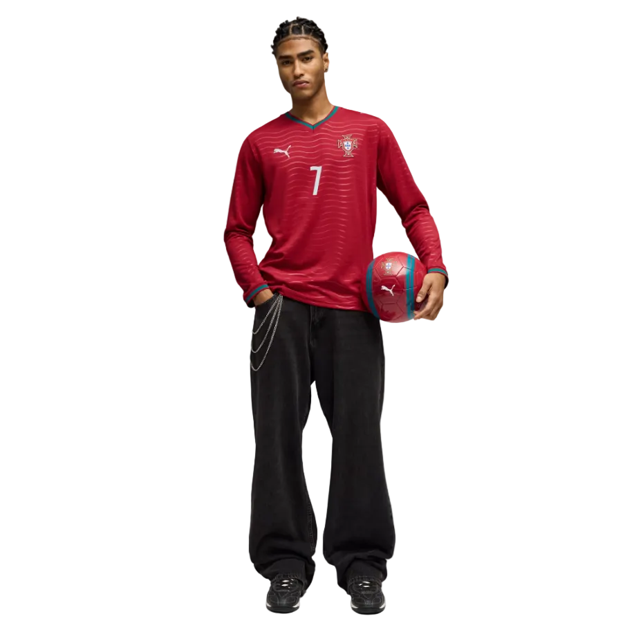A man in a red long-sleeve Portugal soccer jersey (number 7) and baggy black jeans with a chain, holding a red soccer ball against a black background.