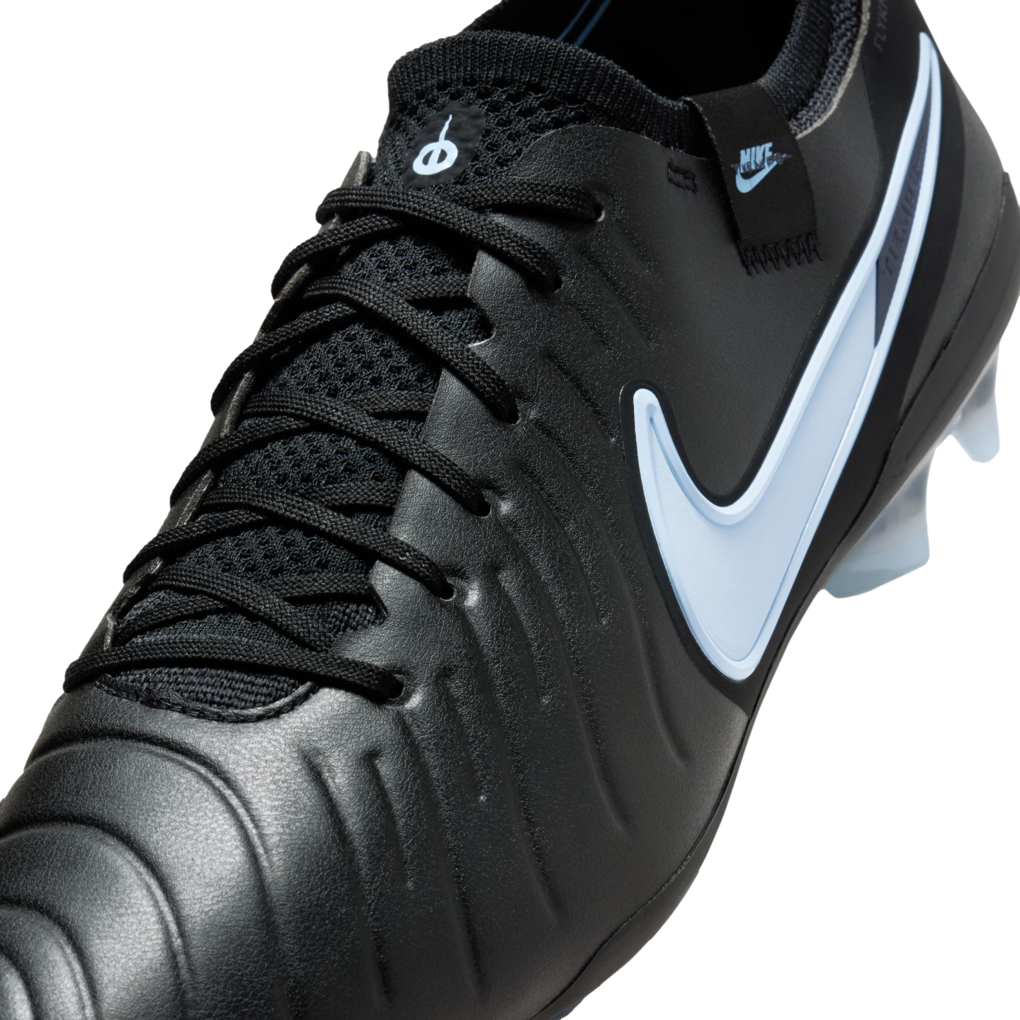 A close-up of a black Nike soccer cleat with a light blue swoosh and textured leather upper, set against a black background.
