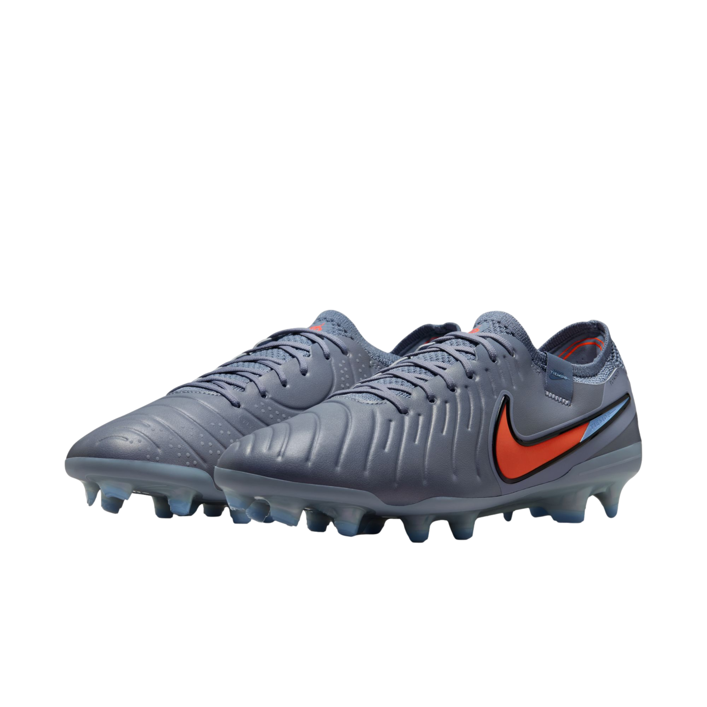 A pair of grey Nike Tiempo soccer cleats with a bright orange swoosh and blue-tinted studs, shown against a solid black background.