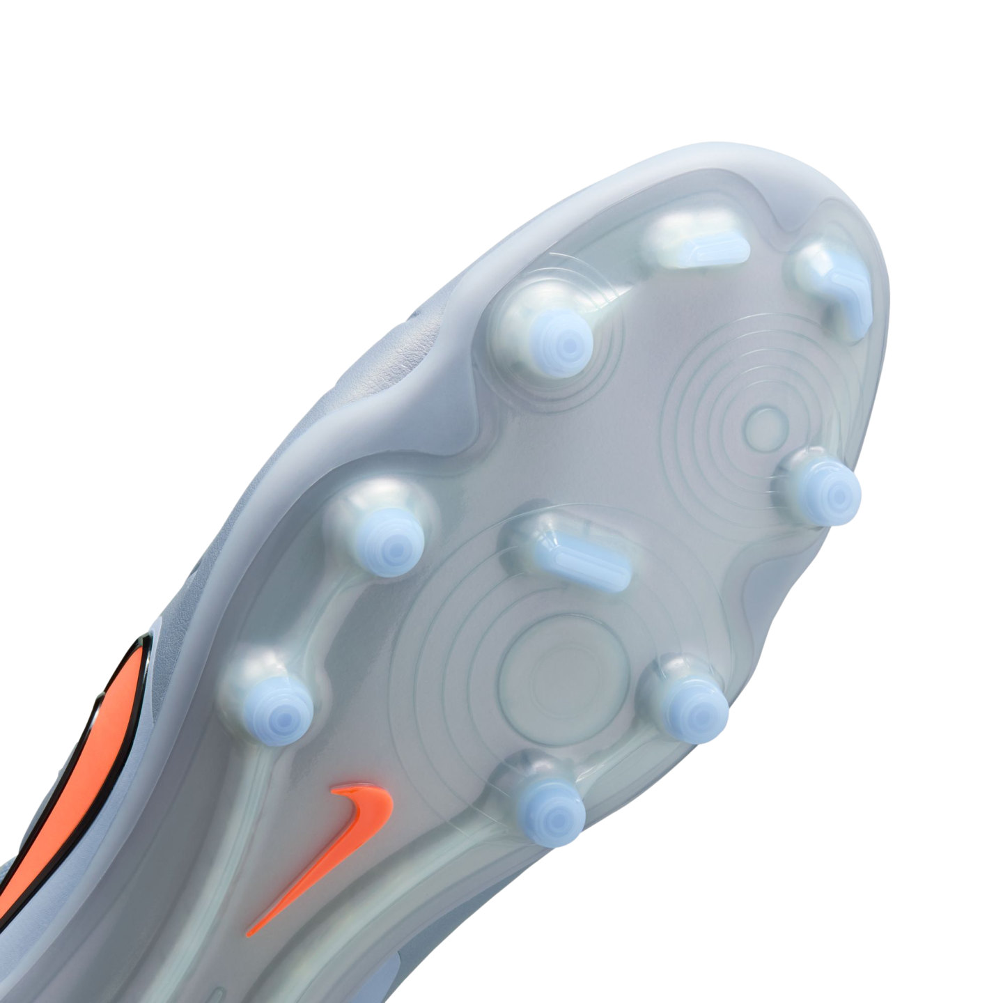 Close-up of the light grey soleplate of a soccer cleat, featuring light blue translucent studs and an orange Nike swoosh against a solid black background.