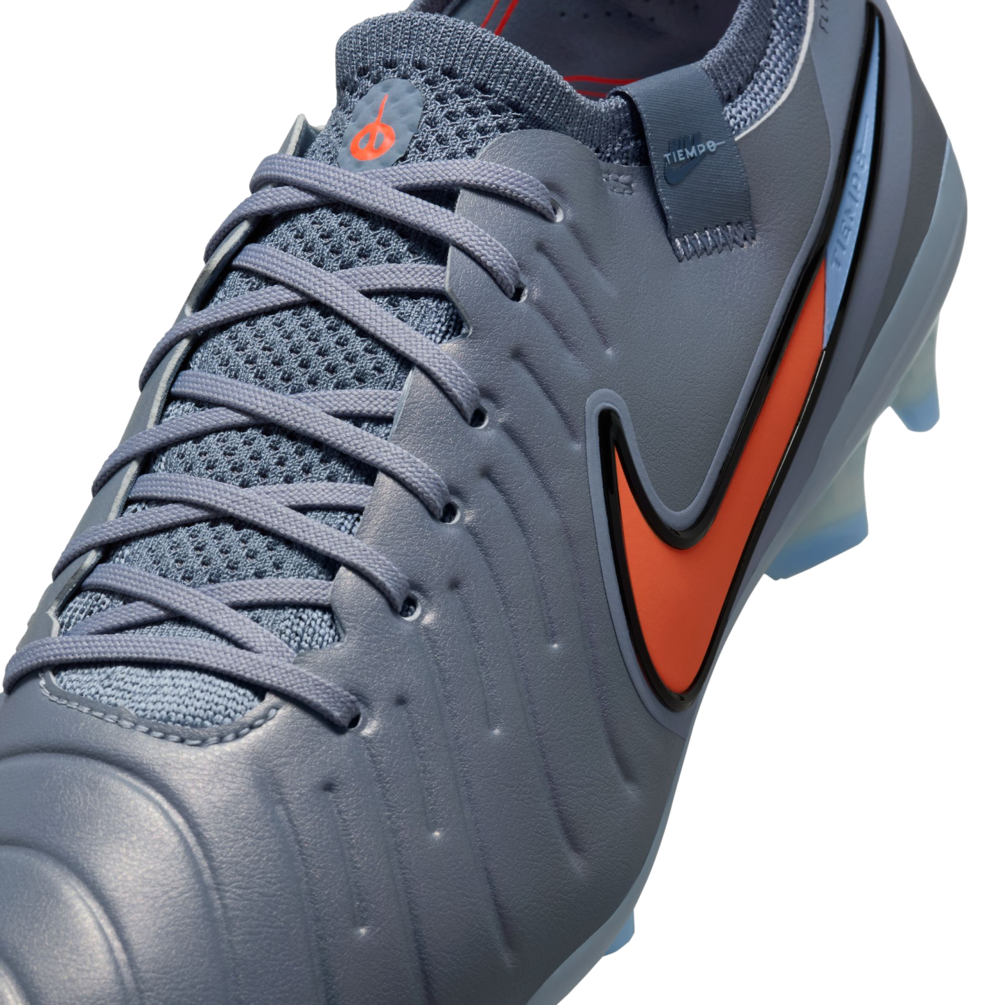 Close-up of a blue-grey Nike Tiempo soccer cleat with a vibrant orange swoosh and matching laces against a black background.