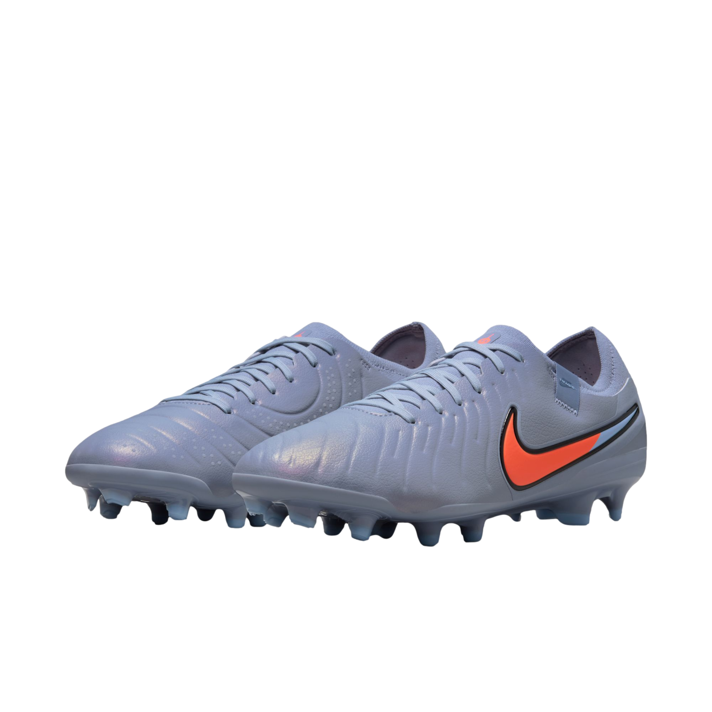 Grey iridescent Nike soccer cleats with a bright orange swoosh on a black background.