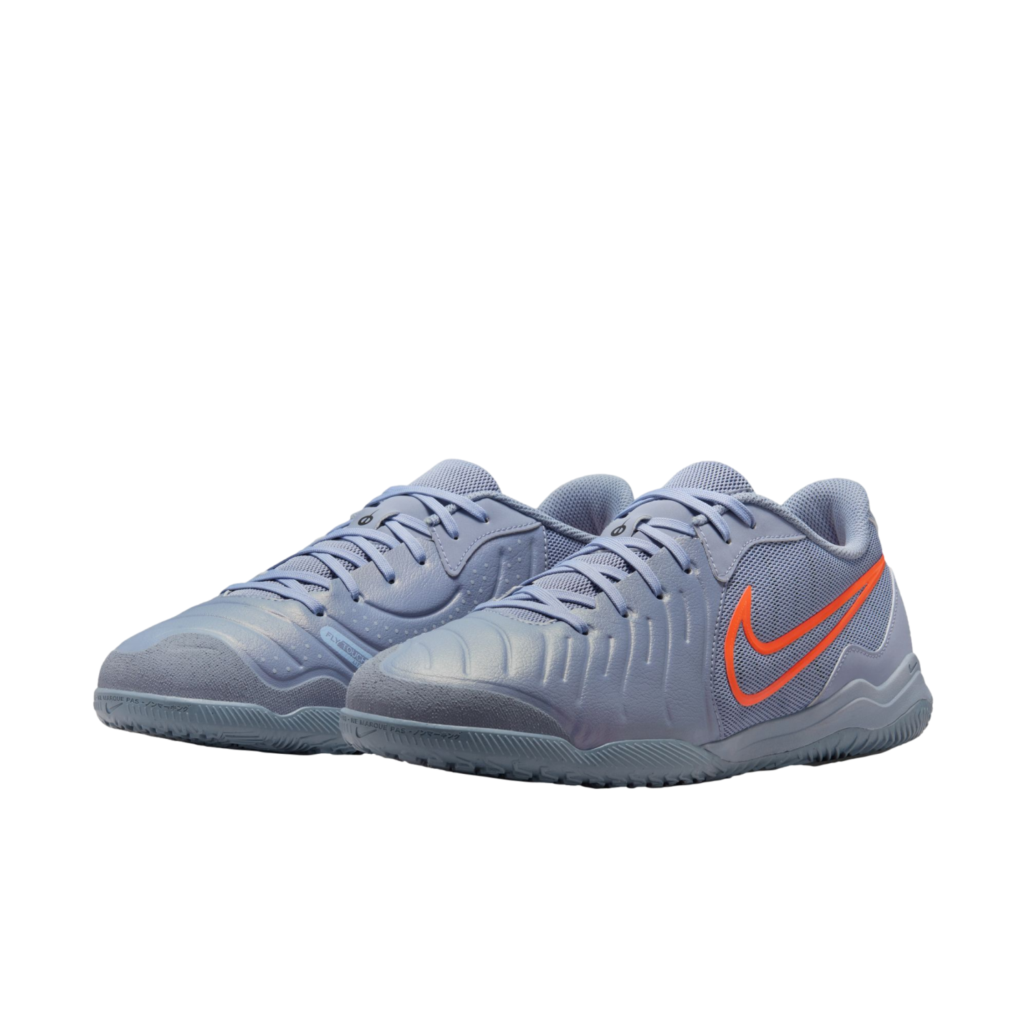 Pair of light purple Nike indoor soccer shoes with a bright orange swoosh logo. They feature a textured upper and flat court soles, shown against a solid black background.