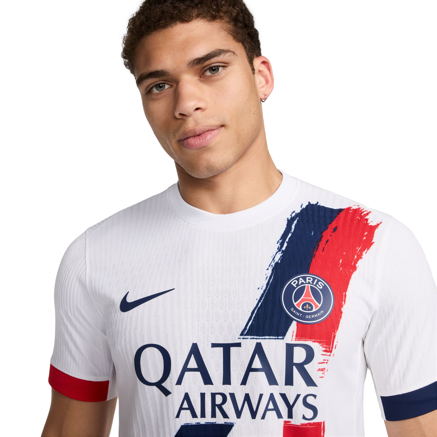 A man posing in a white Nike Paris Saint-Germain (PSG) away jersey featuring a blue and red brushstroke design and the Qatar Airways sponsor logo.