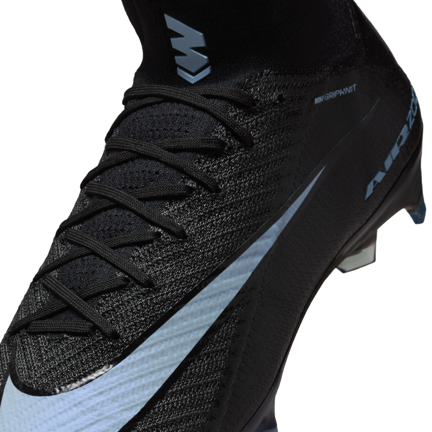 Close-up of a black Nike Mercurial soccer cleat with light blue accents, featuring a textured Gripknit upper, black laces, and an "M" logo on the high-top collar.
