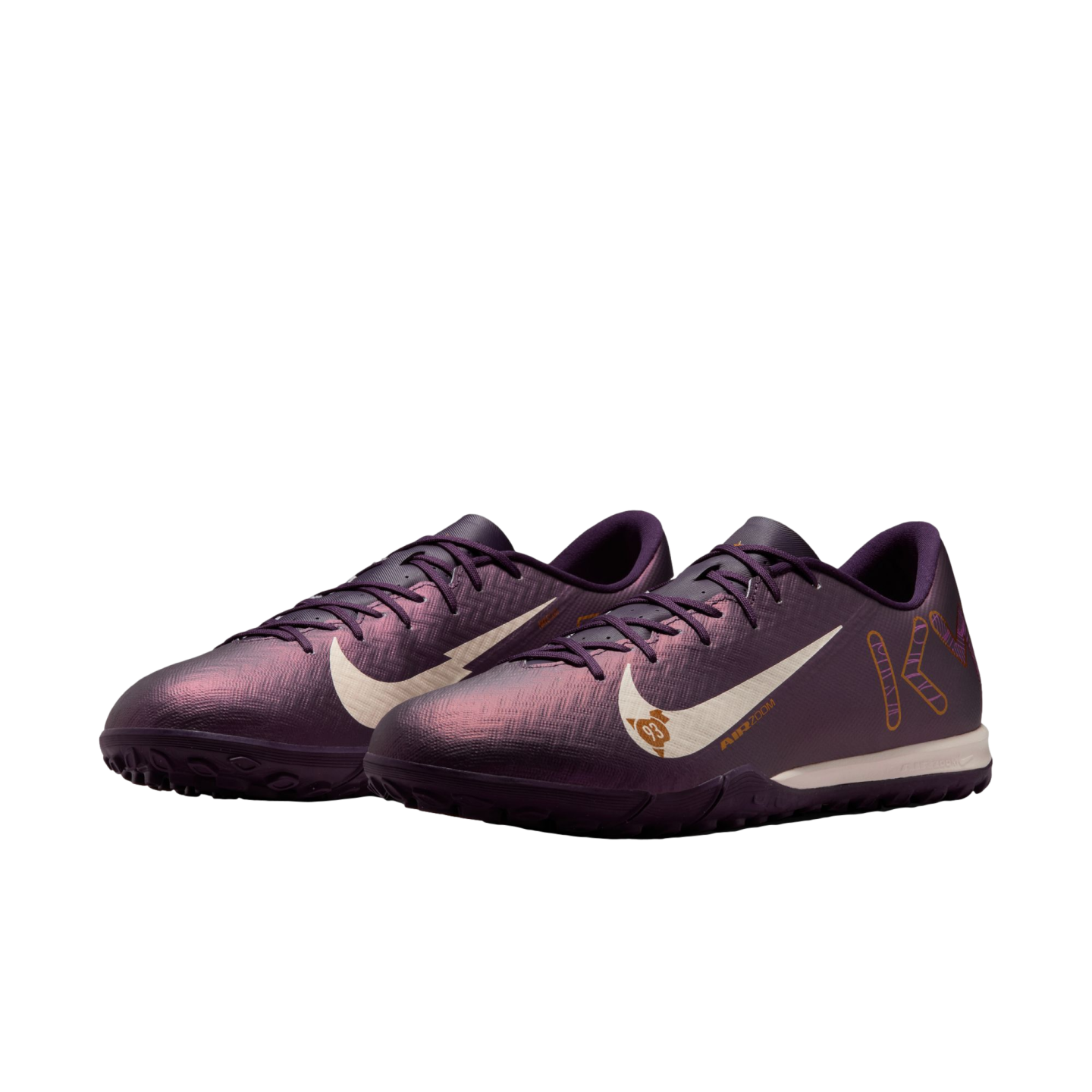A pair of iridescent purple Nike turf soccer shoes featuring white swooshes and gold graphic details.
