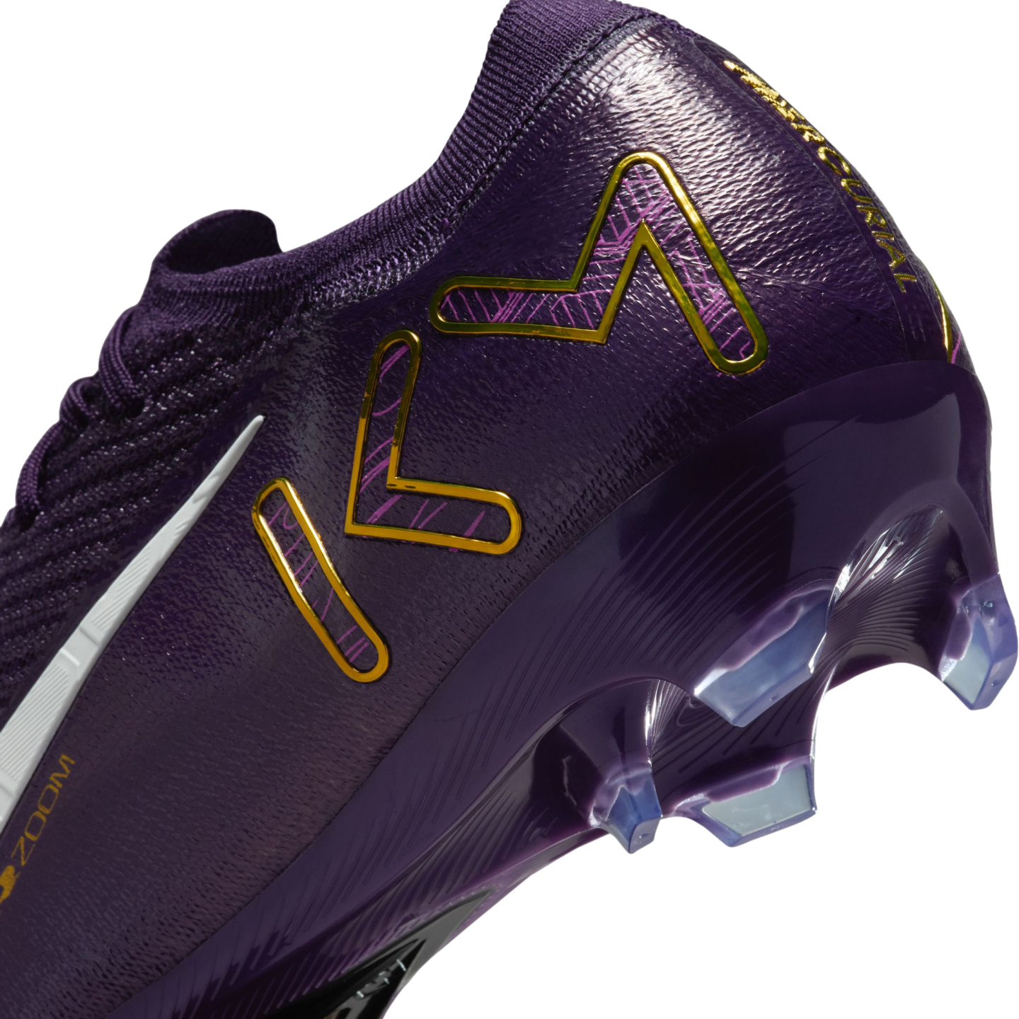 Close-up of the heel of a purple Nike soccer cleat with gold "KM" branding and clear, translucent studs.