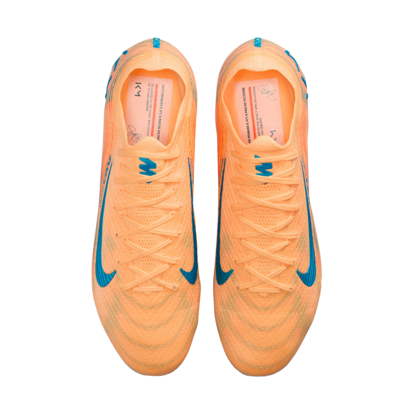 Top-down view of bright orange Nike soccer cleats with blue swoosh accents and Kylian Mbappé "KM" branding on the insoles.