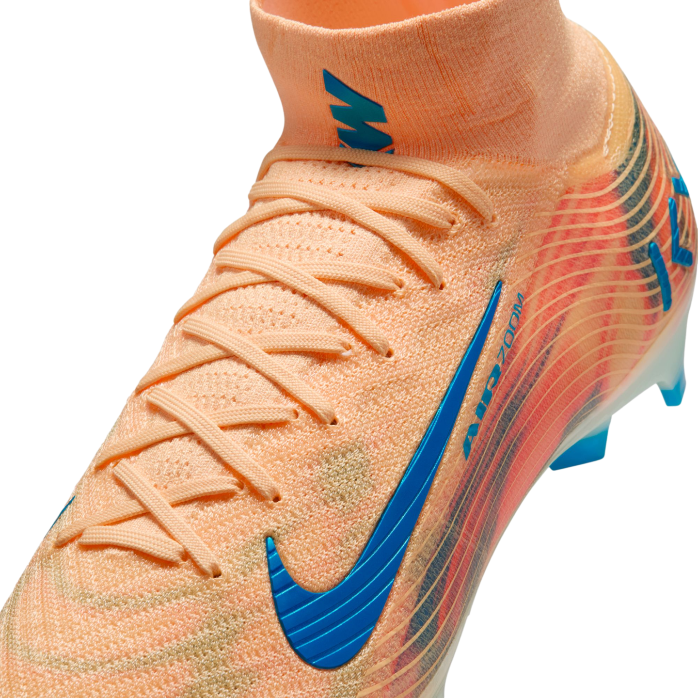 Close-up of a peach Nike soccer cleat featuring a blue swoosh and "AIR ZOOM" branding, with a high-top knit collar and laces against a black background.