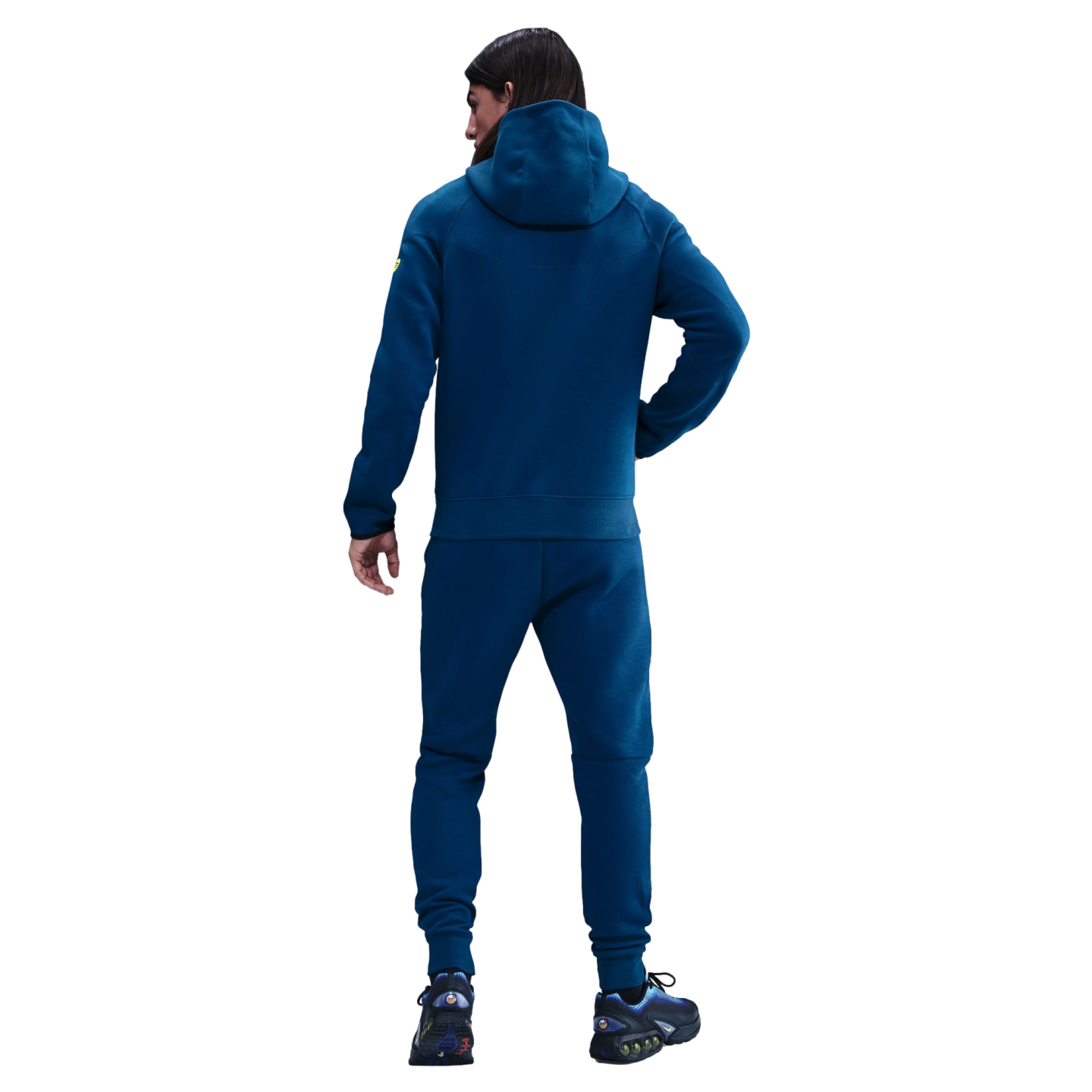 Back view of a person wearing a teal hoodie and matching sweatpants with blue sneakers, against a solid black background.