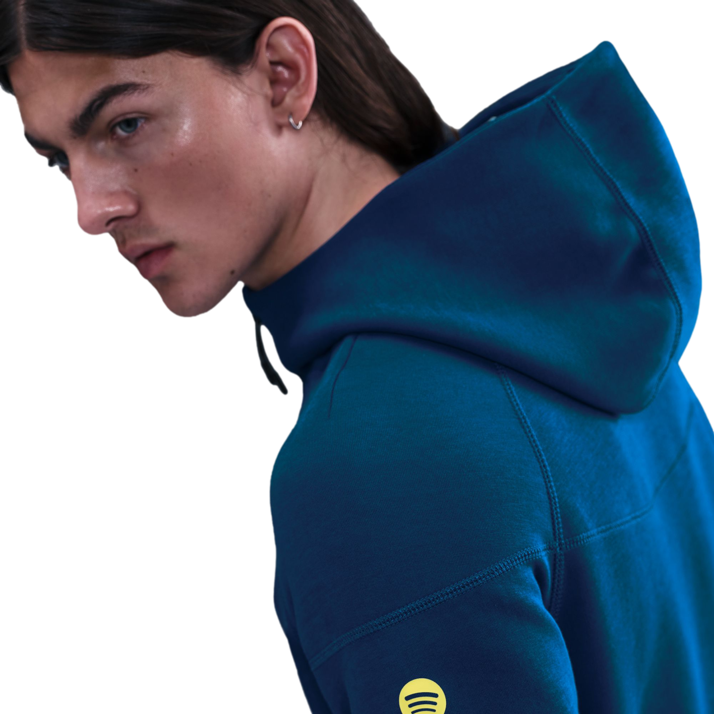 Profile of a person with long hair wearing a dark teal hoodie with a yellow Spotify logo on the sleeve against a black background.