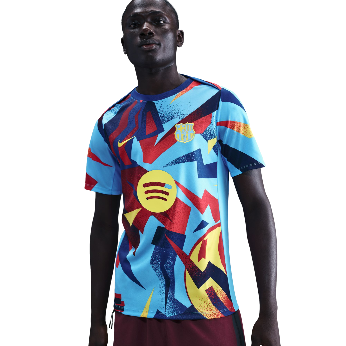 A man wearing an FC Barcelona pre-match jersey with a light blue base and bold, abstract patterns in red, yellow, and dark blue. Features include the Nike swoosh and Spotify logo.