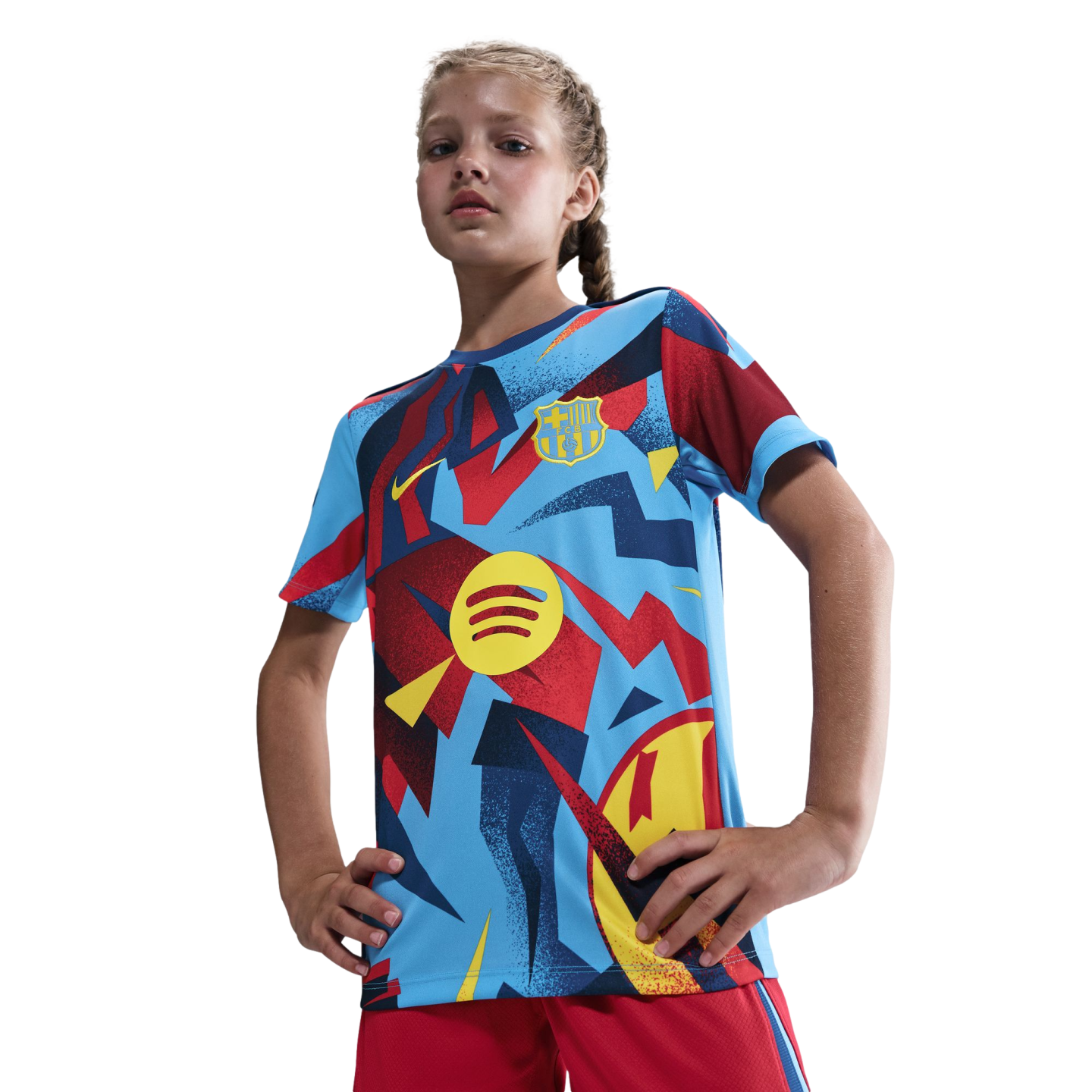 A young girl poses in a vibrant blue, red, and yellow patterned FC Barcelona soccer jersey featuring the Spotify logo against a black background.