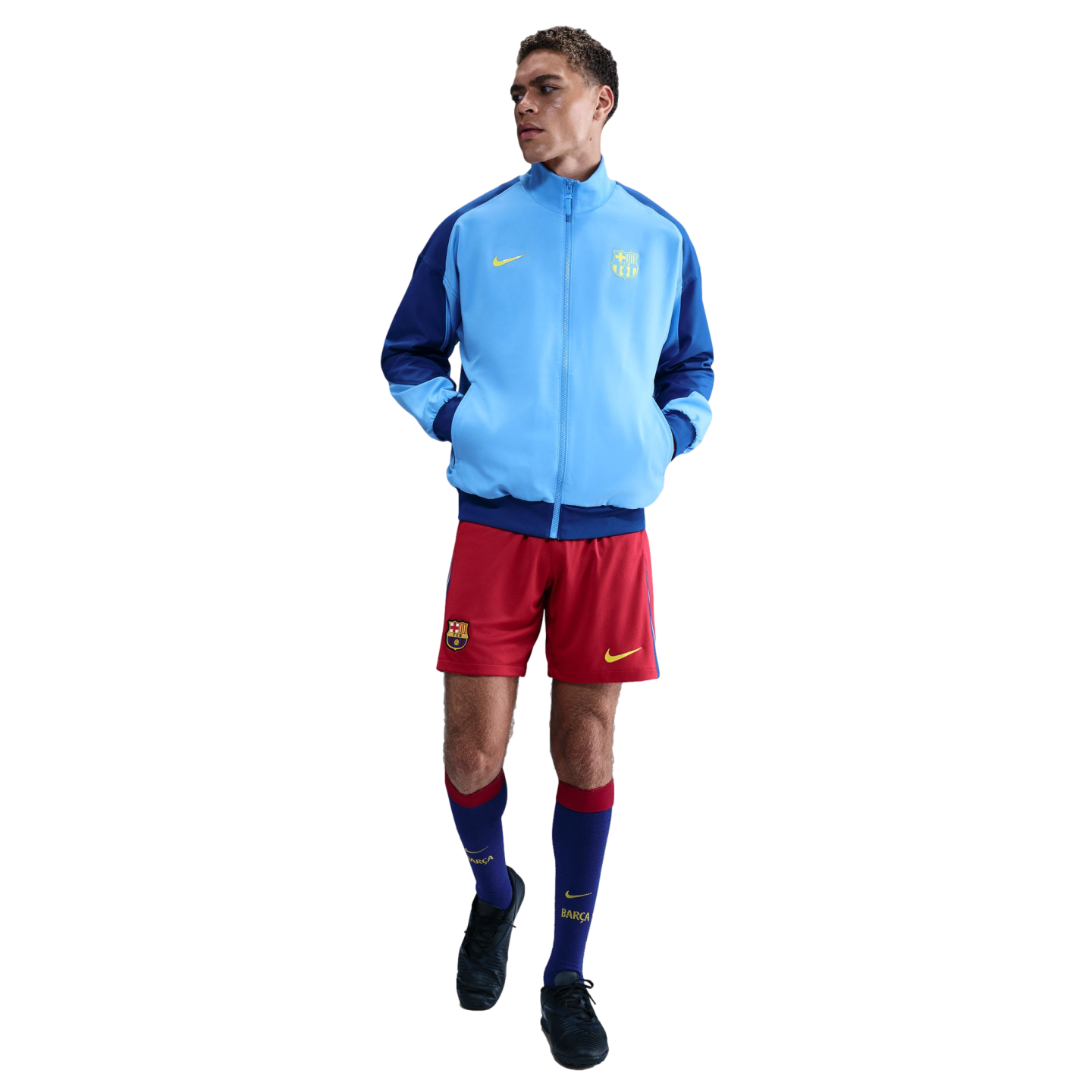 Man modeling a light blue and navy FC Barcelona track jacket, red shorts, and tall blue socks against a solid black background.