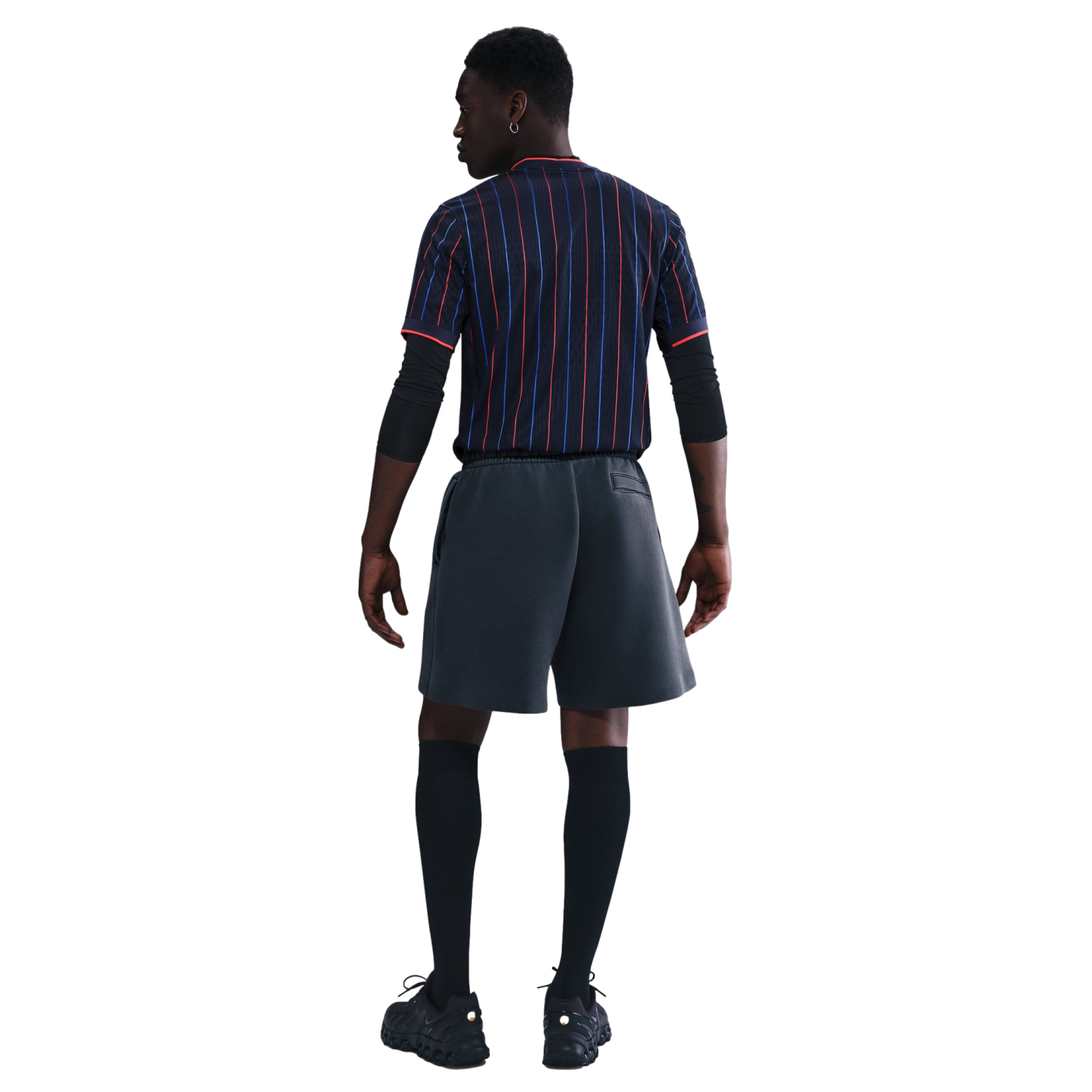 A full-body rear view of a model wearing a dark pinstriped jersey, black athletic arm sleeves, charcoal gray athletic shorts, black knee-high socks, and black sneakers against a white background.