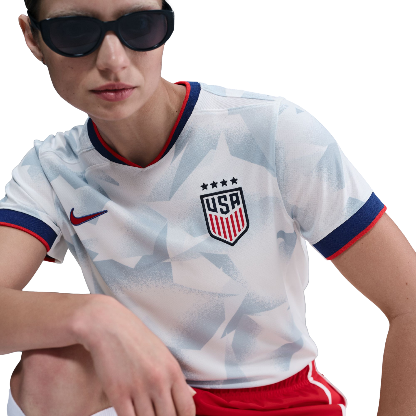 A person wearing a white USA soccer jersey with a blue star pattern, red and blue trim, and four stars above the USA crest, paired with dark sunglasses.