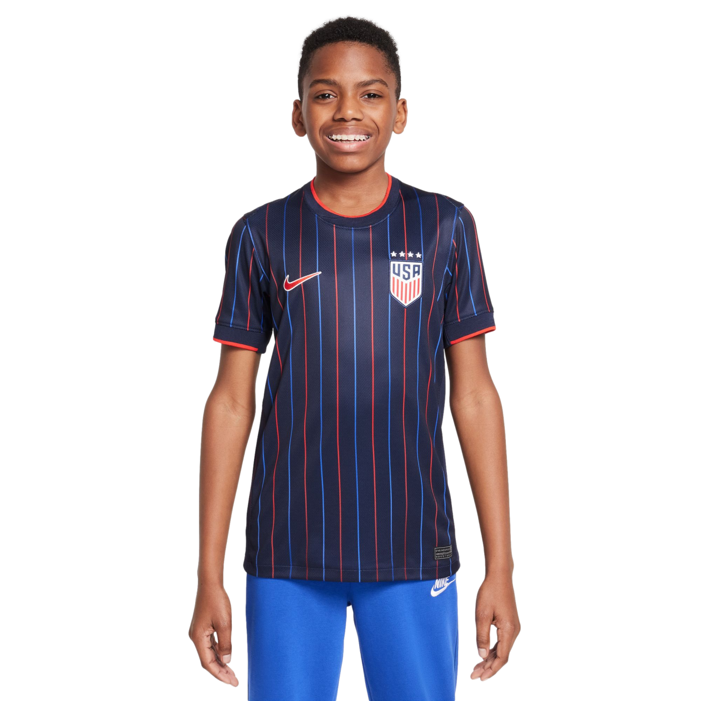 A smiling boy wearing a navy blue USA soccer jersey with red and blue pinstripes and blue sweatpants against a white background.