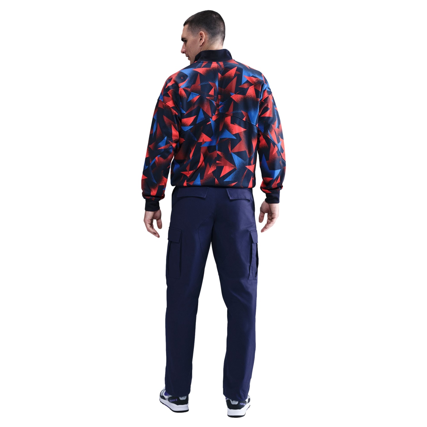 Rear view of a man wearing a red and blue geometric print jacket and navy cargo pants.