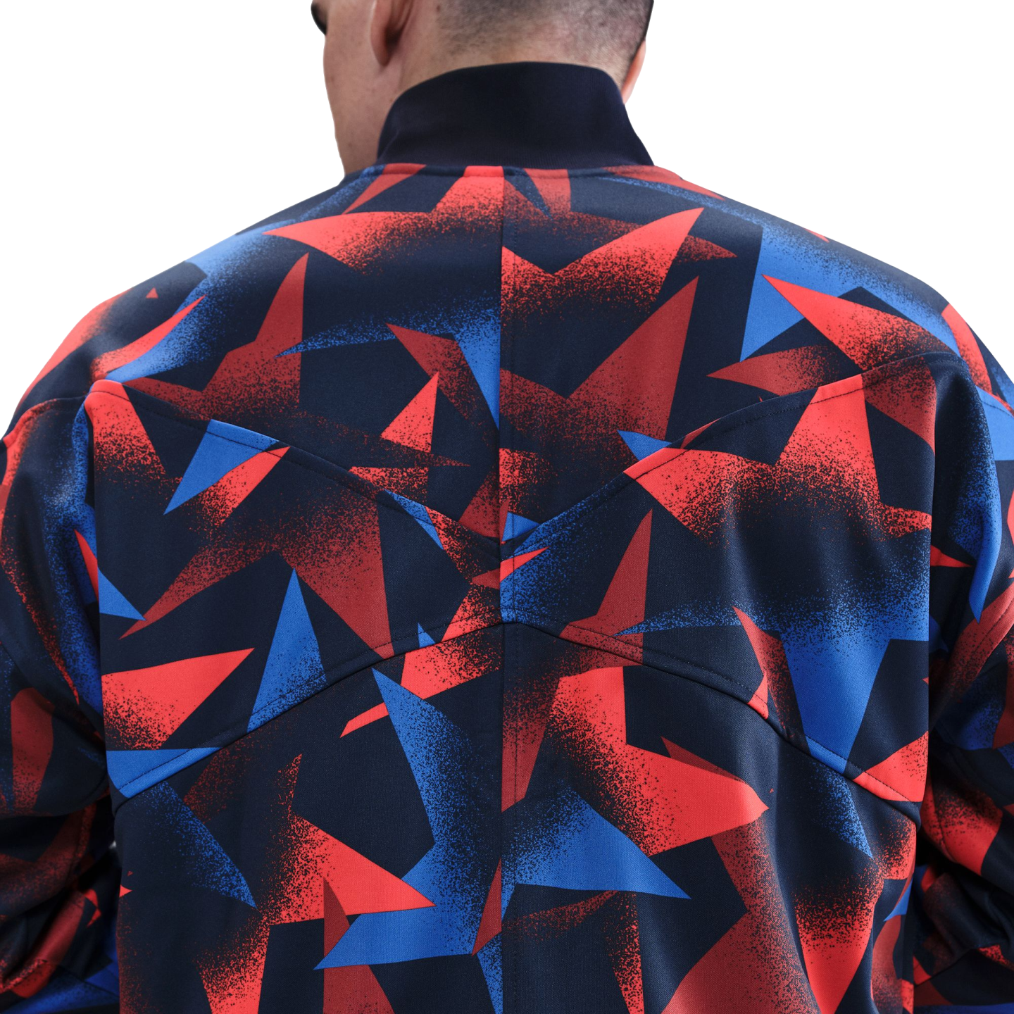 Rear view of a person wearing a jacket with a graphic red, blue, and black geometric pattern. The jacket has a high black collar and visible back seams.