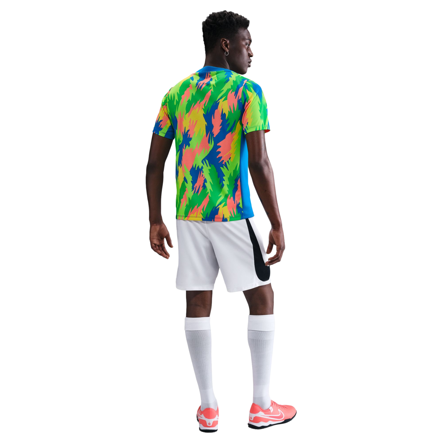 Rear view of a Black man in a colorful patterned jersey, white shorts, long white socks, and pink sneakers against a plain white background.