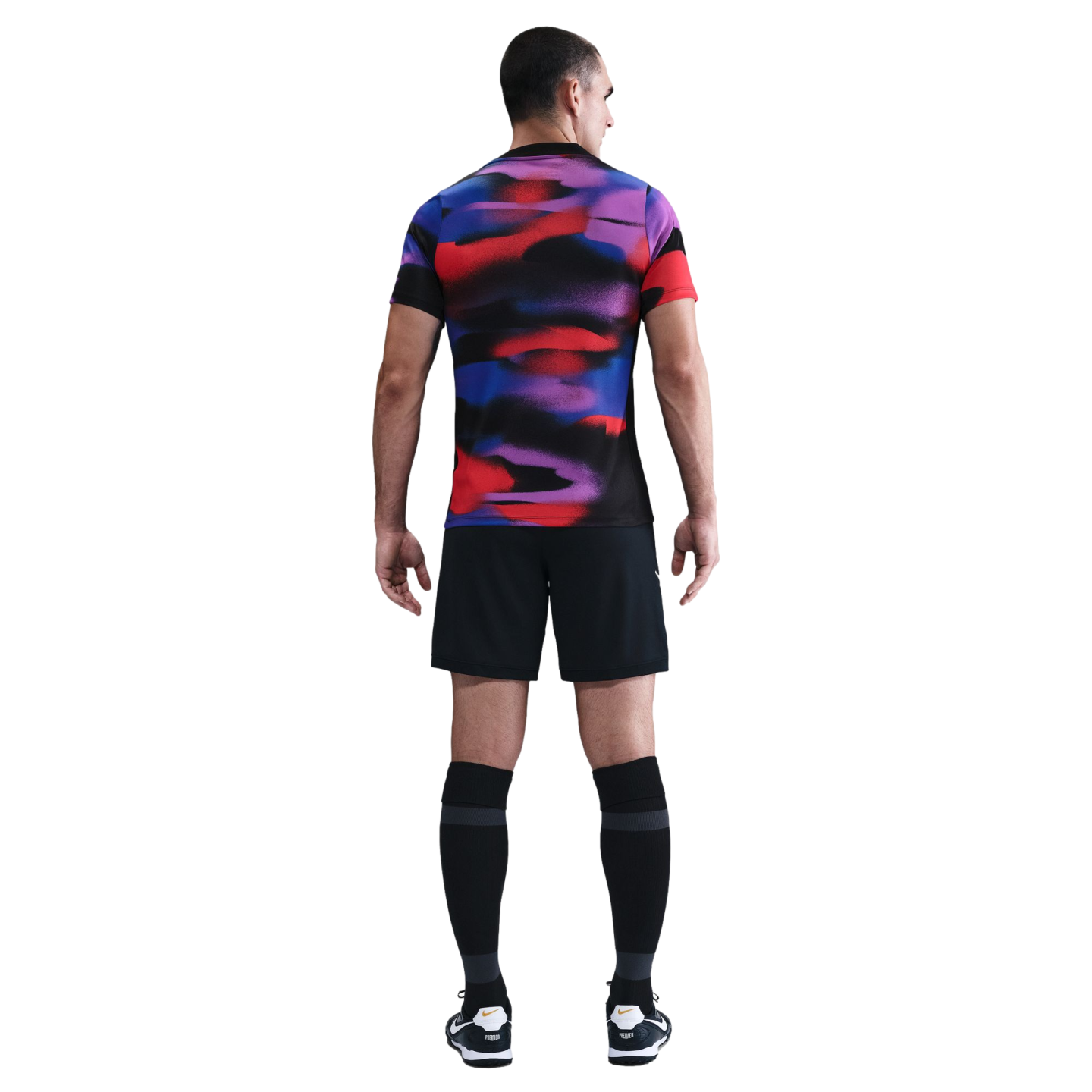 Rear view of a man wearing a vibrantly patterned multicolored sports jersey, black shorts, and tall black socks against a white background.