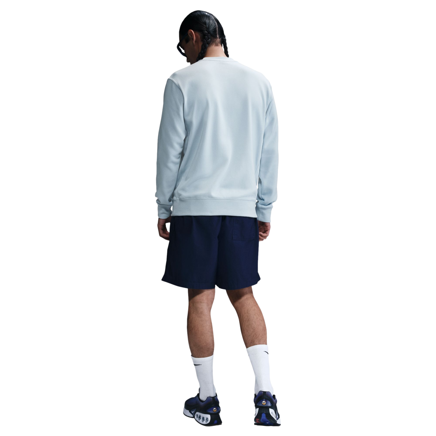 Back view of a person wearing a light blue sweatshirt, navy shorts, and white socks with blue sneakers, standing against a plain white background.