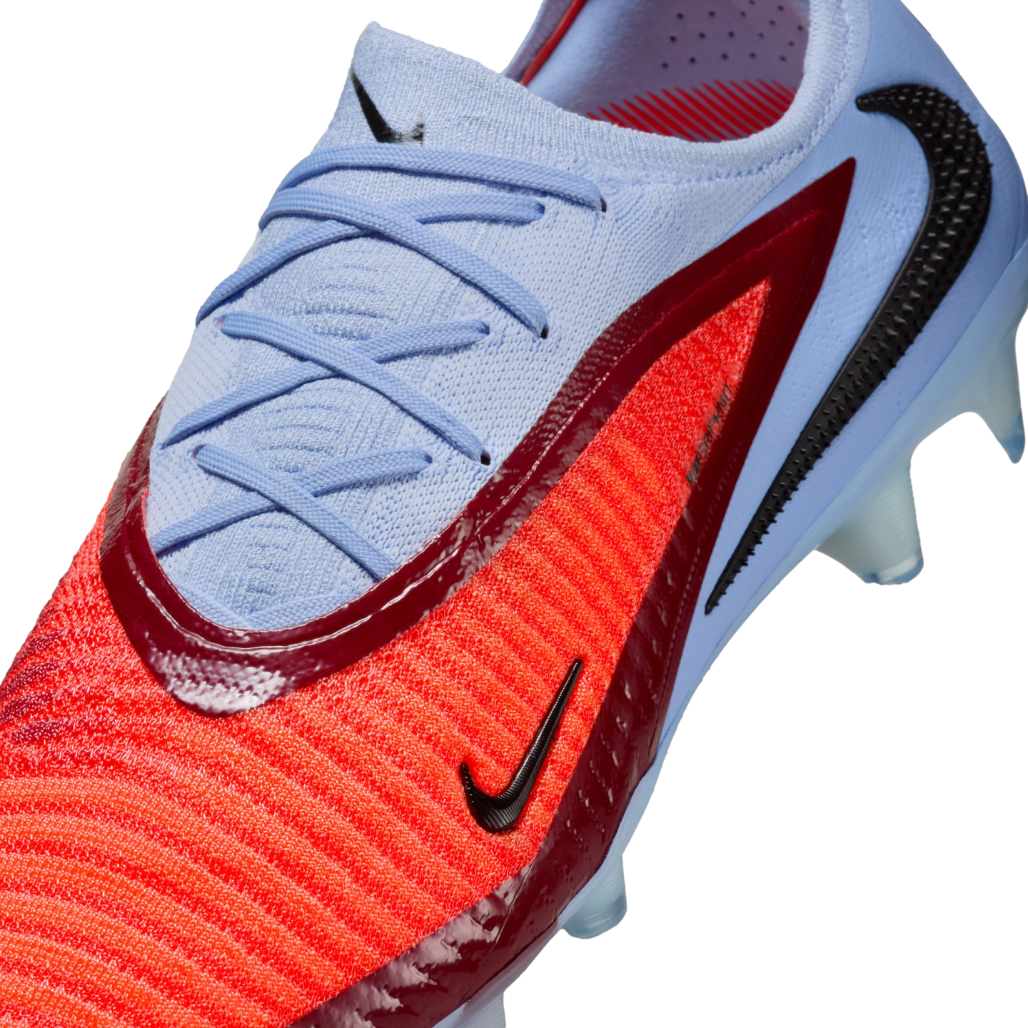 Close-up of a Nike soccer cleat featuring light blue knit upper and laces, a bright orange textured forefoot, and dark red glossy accents.