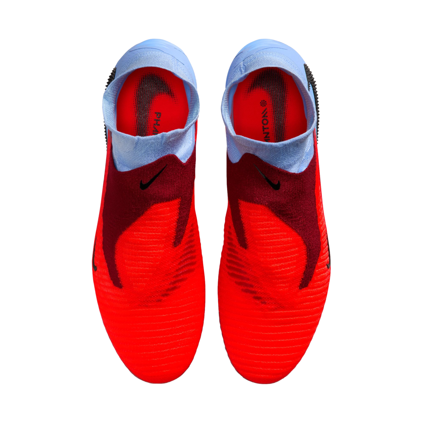A top-down view of a pair of red and light blue laceless Nike Phantom football boots against a solid black background.