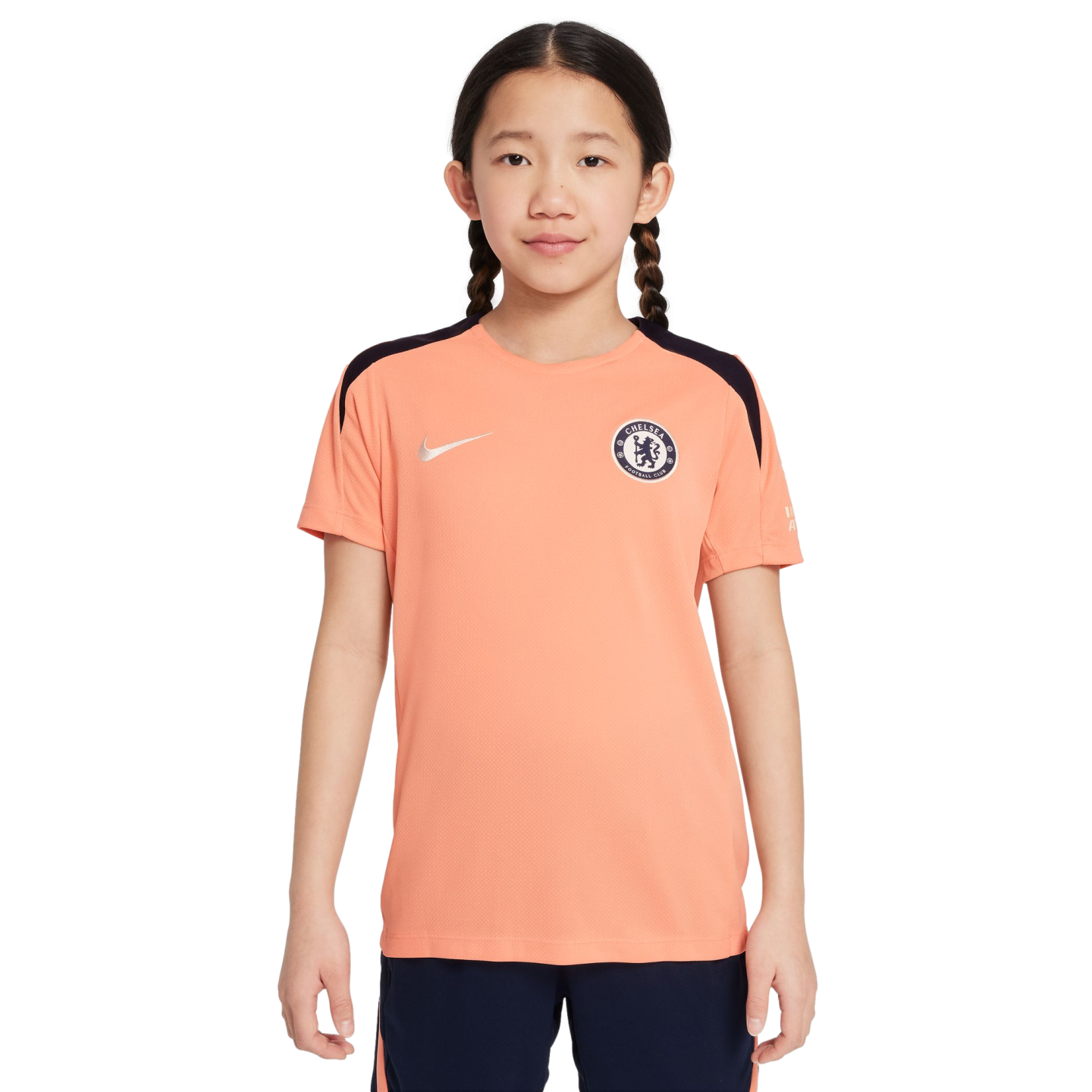 Young girl with braids wearing a peach Chelsea FC Nike soccer jersey and navy shorts on a white background.