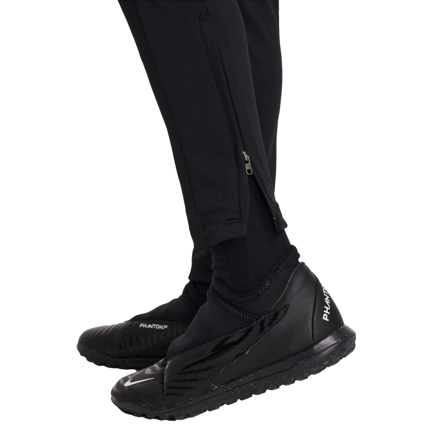 Close-up of a person wearing all-black Nike athletic gear, including Phantom GT turf shoes, socks, and tapered pants with ankle zippers.