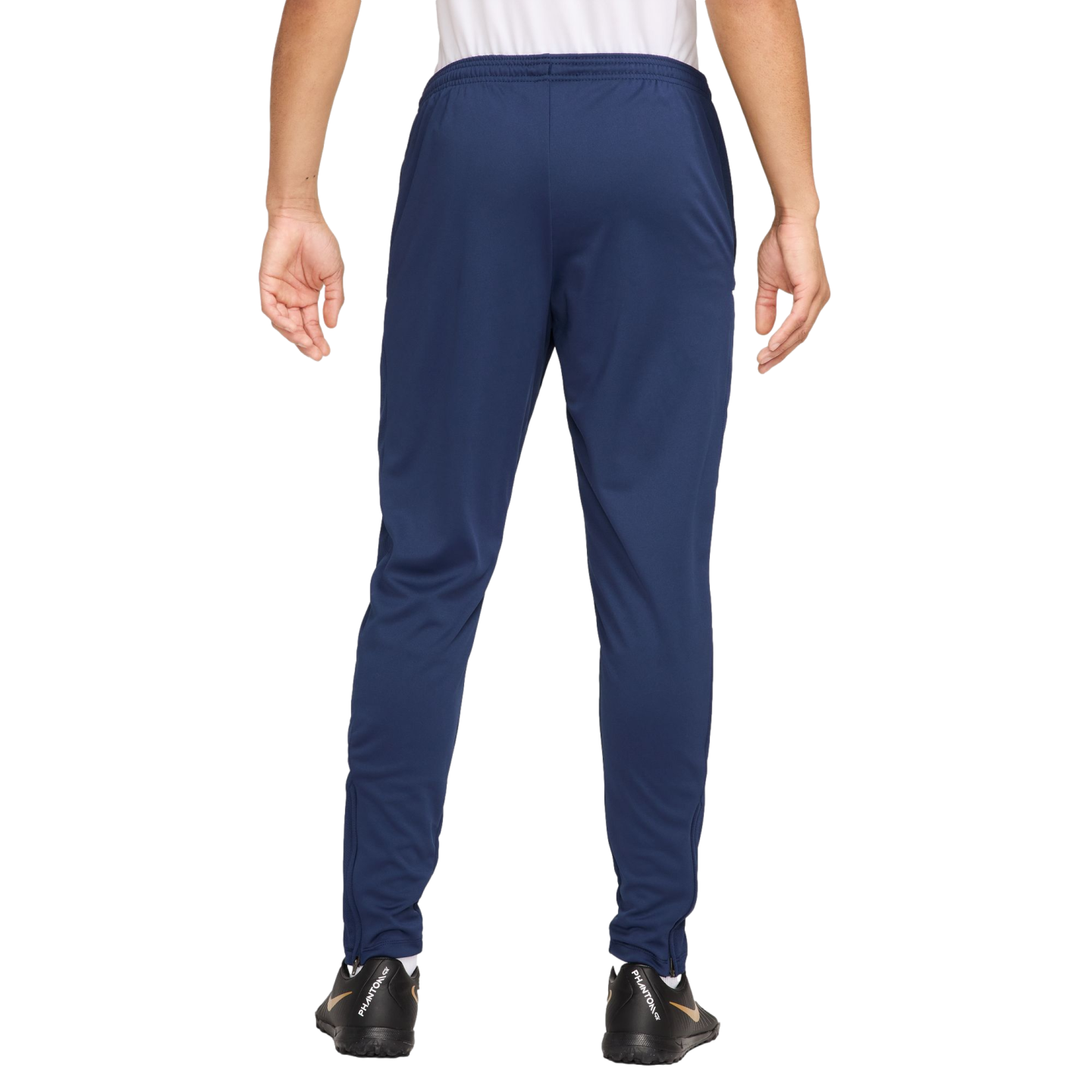 Rear view of a person wearing navy blue track pants and black soccer shoes against a plain white background.