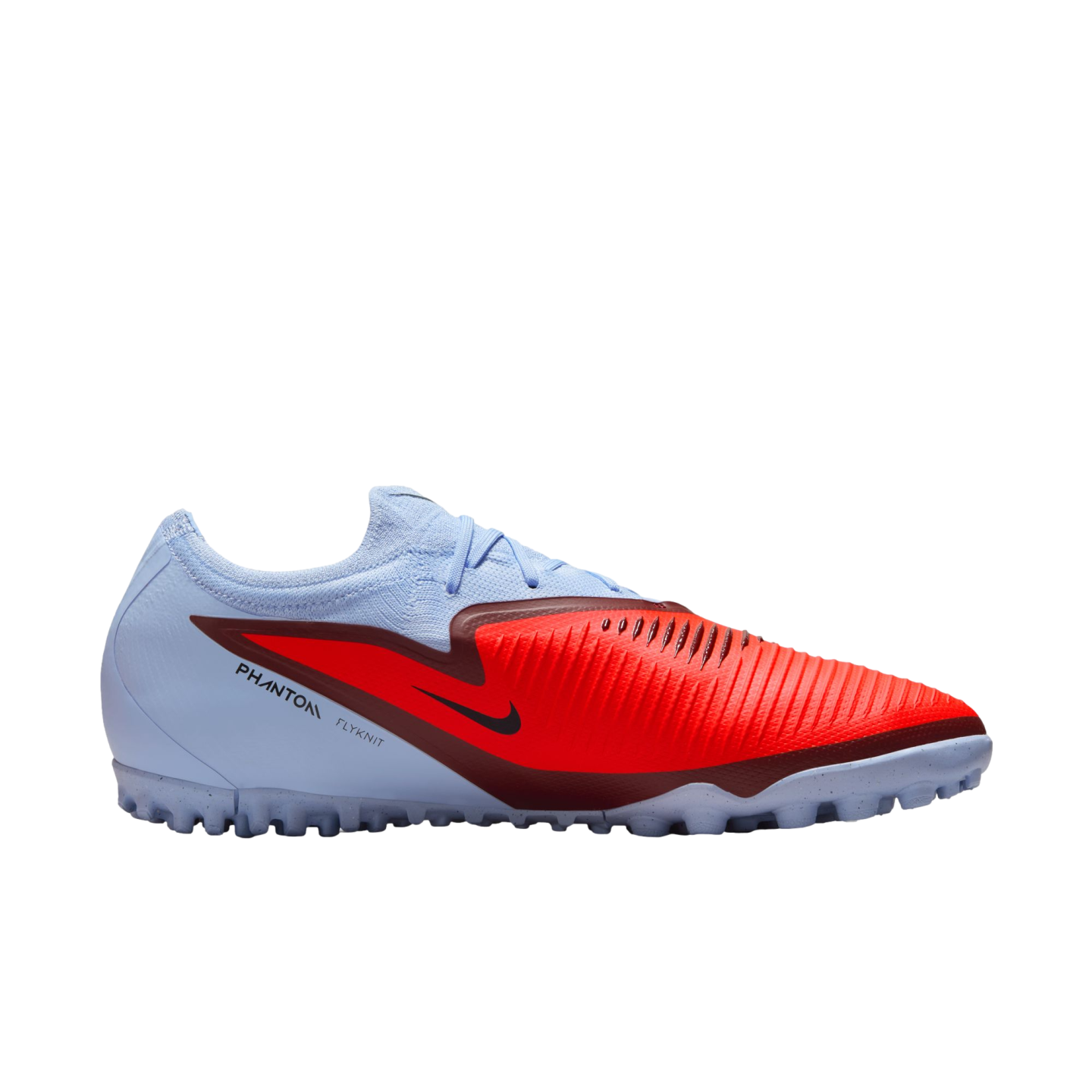 A side view of a light blue and red Nike Phantom Flyknit turf soccer shoe with a textured striking zone and maroon accents, isolated on a black background.