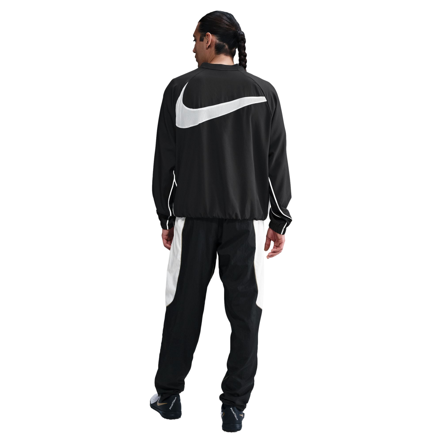 Back view of a man in a black Nike tracksuit featuring a large white swoosh on the jacket and white panels on the pants against a white background.