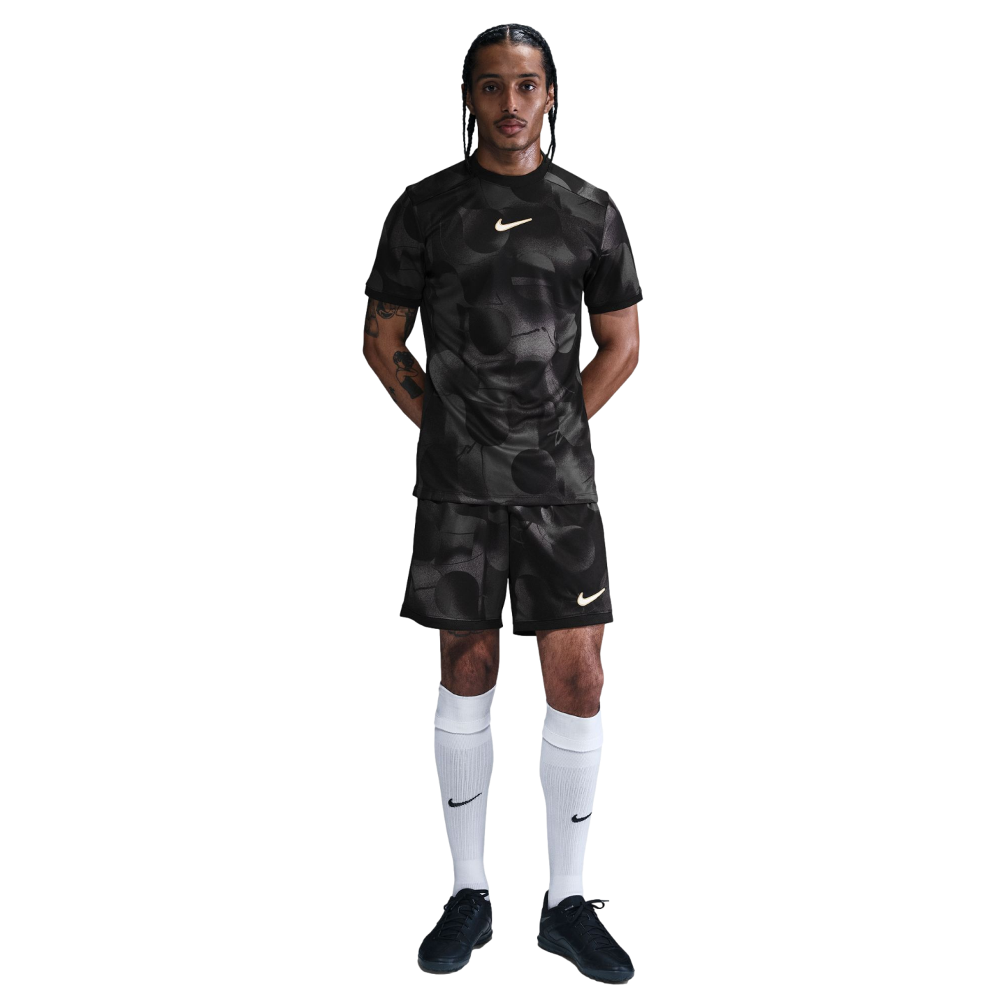 Man in a black patterned Nike soccer uniform with white knee-high socks and black shoes, standing against a plain white background.