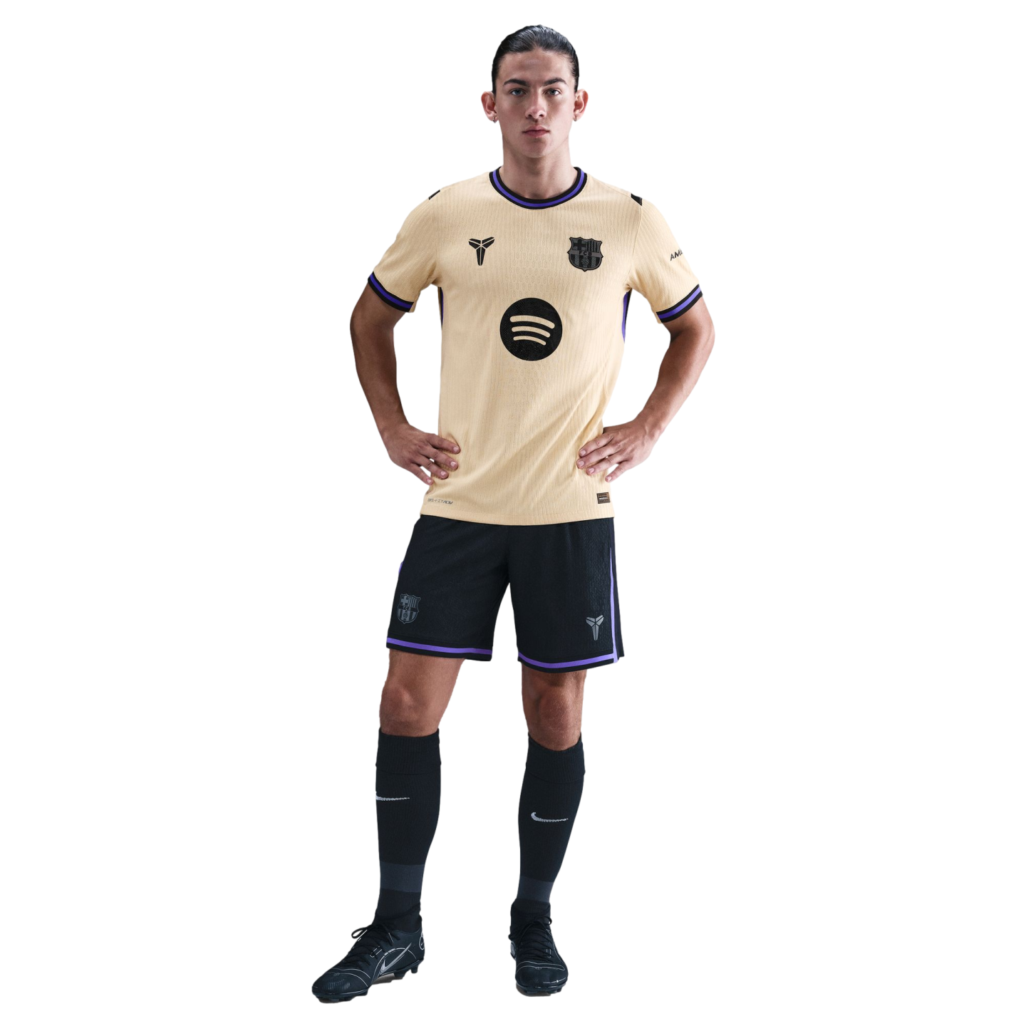 A man wearing a gold and purple FC Barcelona soccer kit featuring Kobe Bryant’s Mamba logo, posed with hands on hips against a black background.