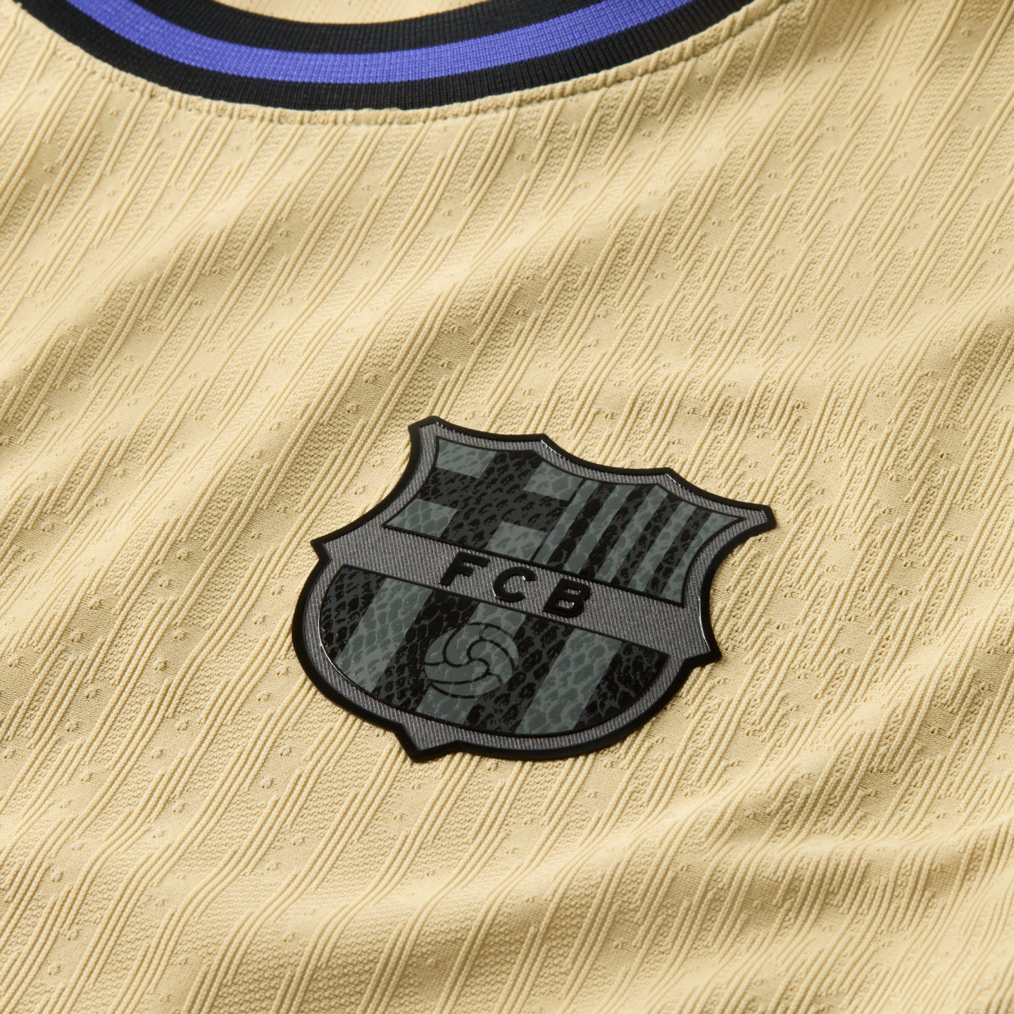 Close-up of a beige textured soccer jersey featuring a monochromatic FC Barcelona crest with a snakeskin pattern and a black and blue striped neckline.
