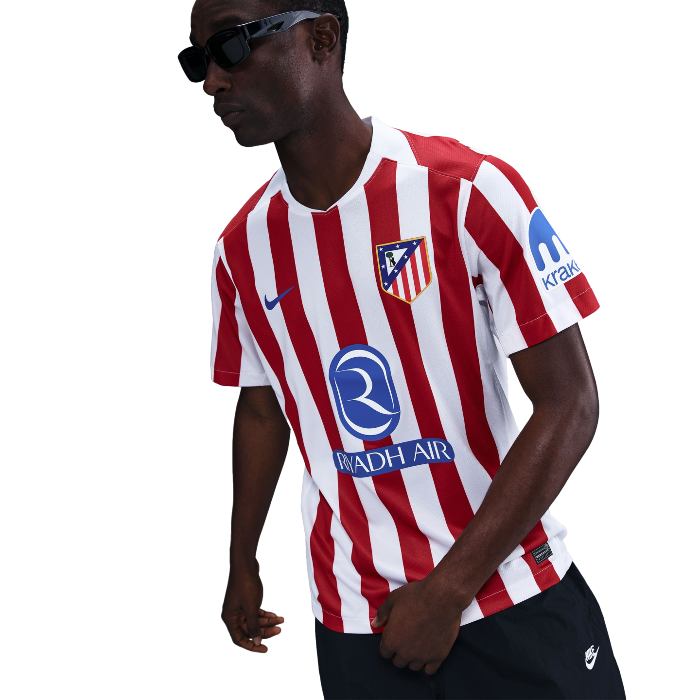 A person in sunglasses wearing a red and white striped Atletico Madrid soccer jersey with Riyadh Air and Kraken sponsors, standing against a white background.