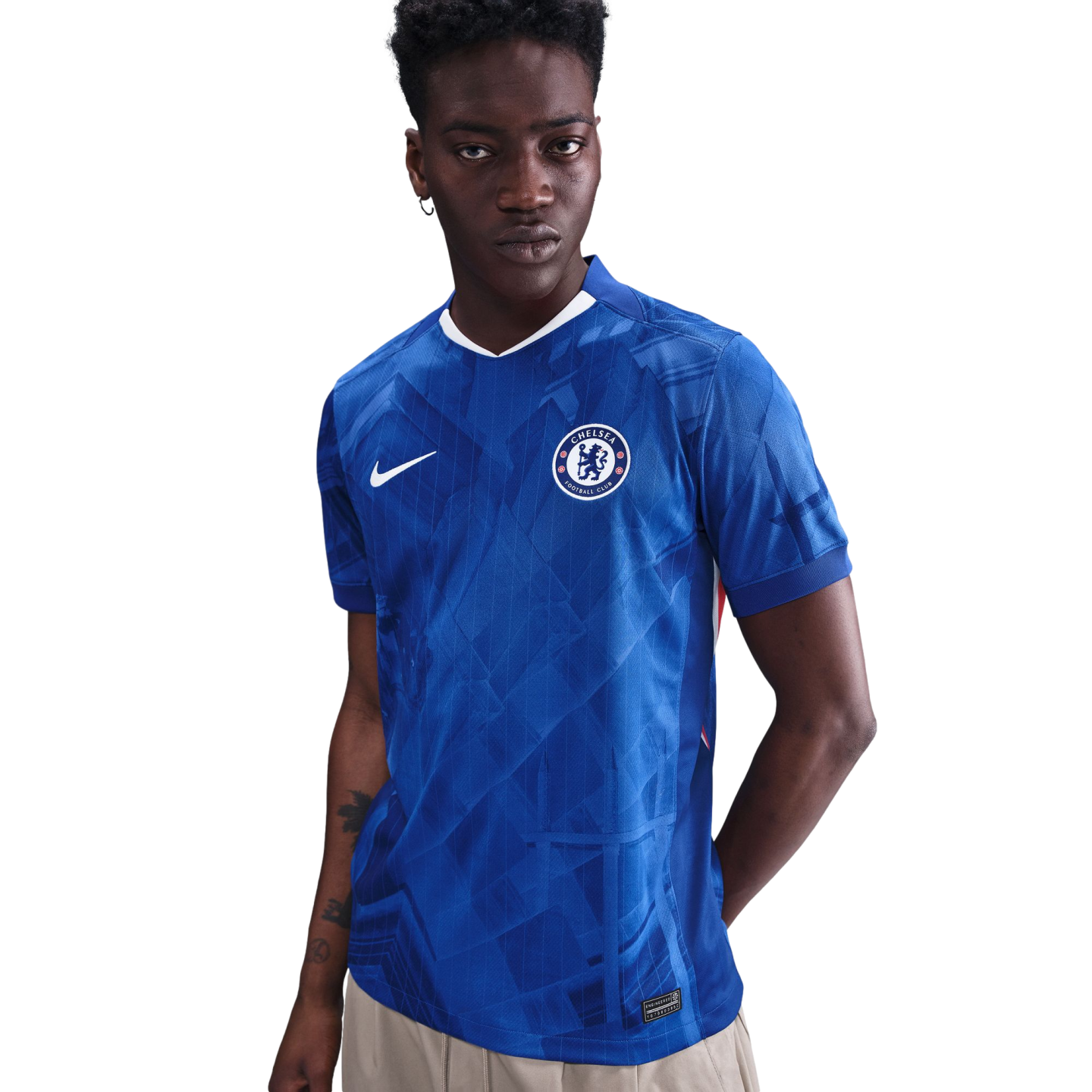 A young man with dark skin wearing a blue Chelsea F.C. soccer jersey with a subtle pattern and white Nike logo, posing against a white background.