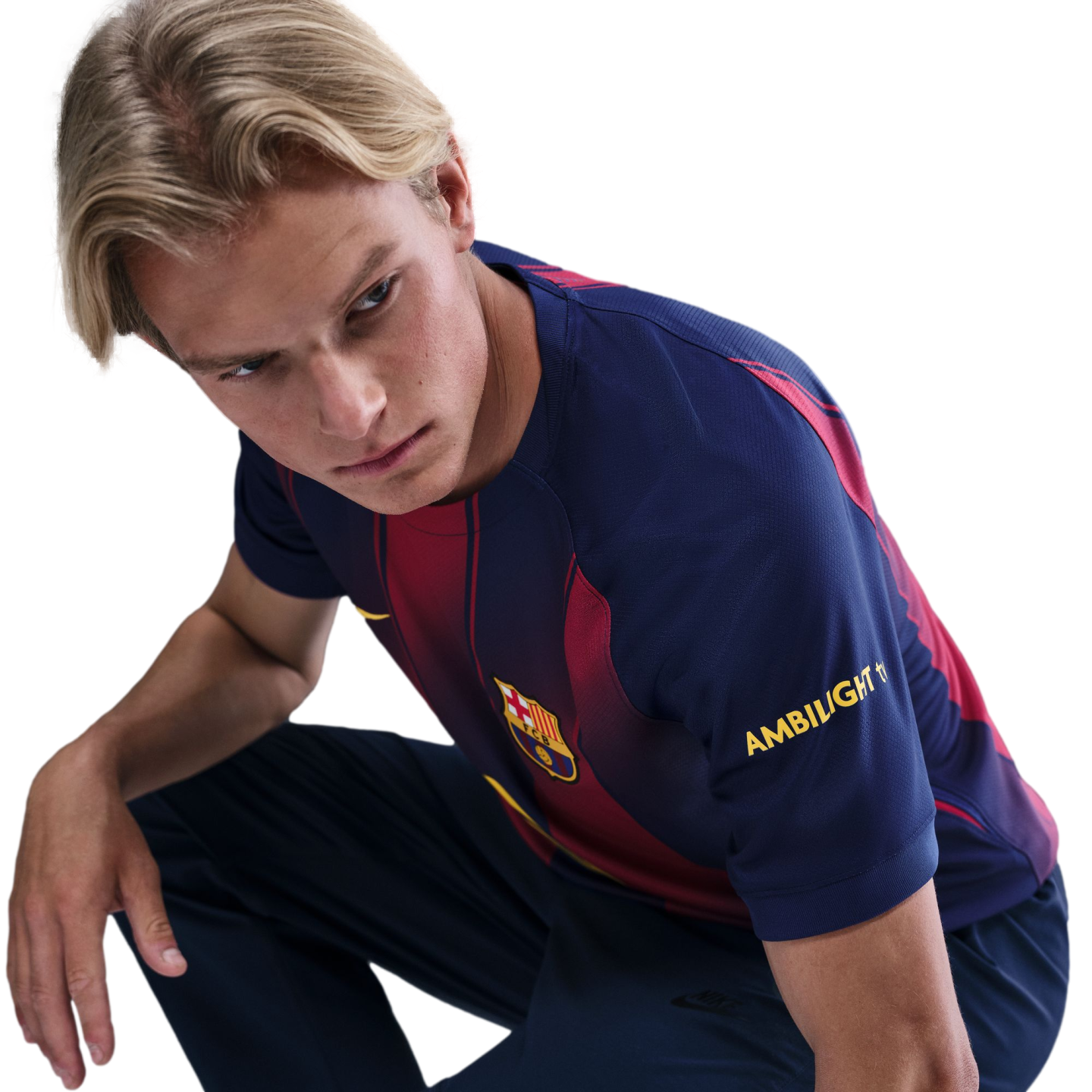 A young man with blonde hair squats and looks intently over his shoulder while wearing an FC Barcelona jersey against a solid black background.