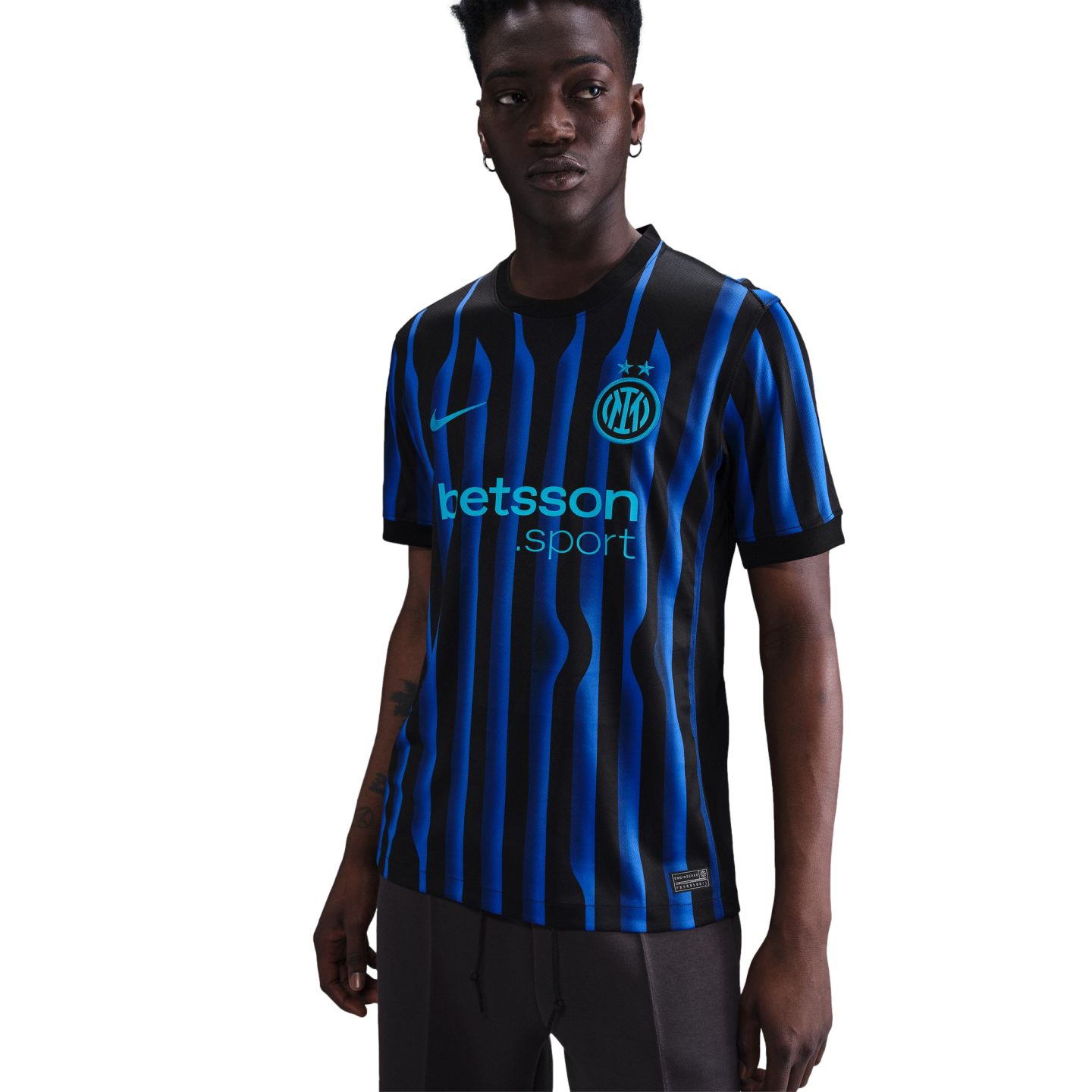 A man models the Inter Milan home jersey featuring black and blue wavy stripes, the Nike swoosh, club crest with two stars, and the Betsson Sport sponsor logo.