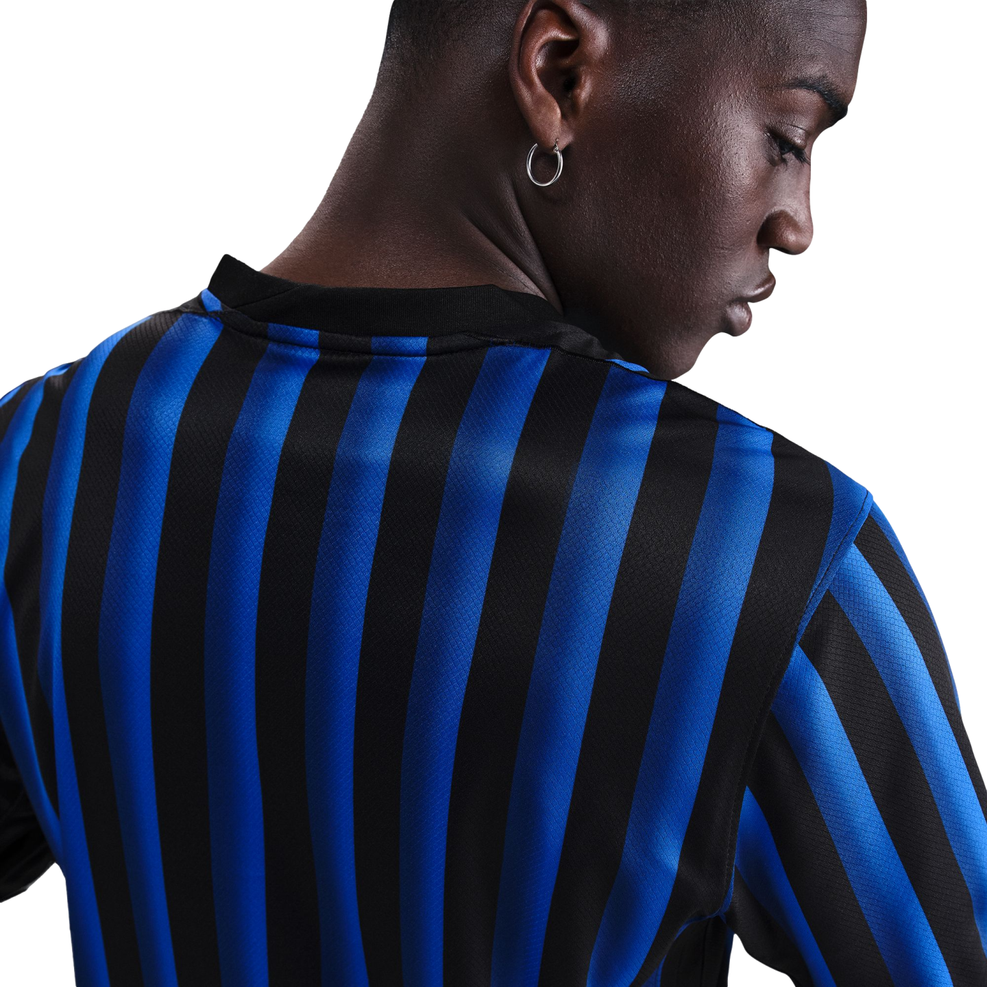 Close-up of a person with dark skin from behind, wearing a blue and black striped jersey and a silver hoop earring.