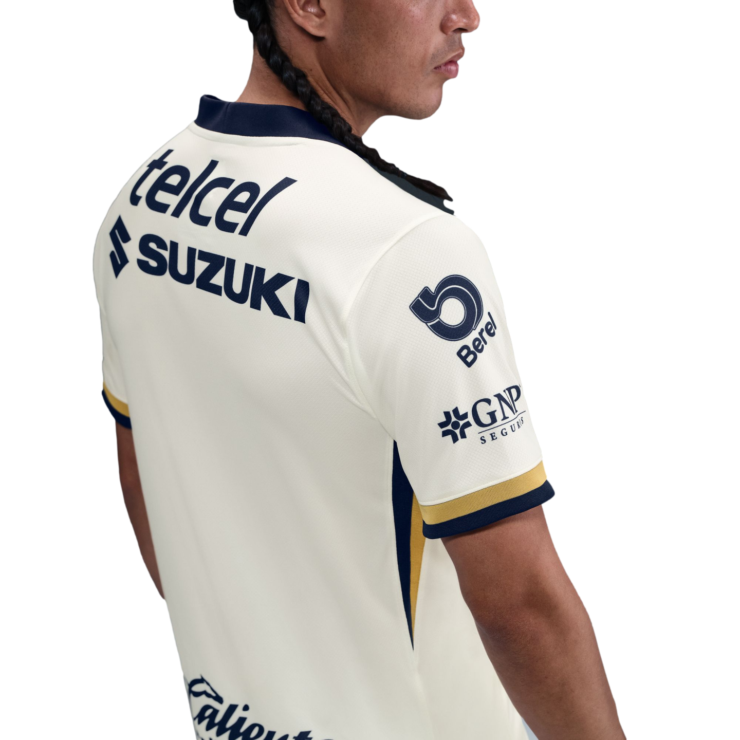 A person with a long braid wearing a white soccer jersey featuring blue and gold trim and sponsor logos including Telcel, Suzuki, and GNP Seguros.