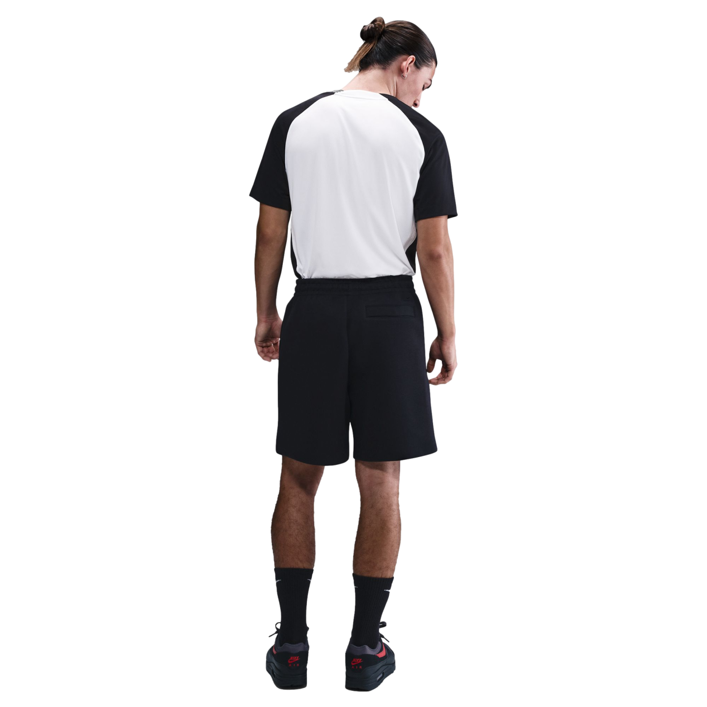 Rear view of a man wearing a black and white raglan T-shirt, black athletic shorts, and black sneakers, standing against a white background.