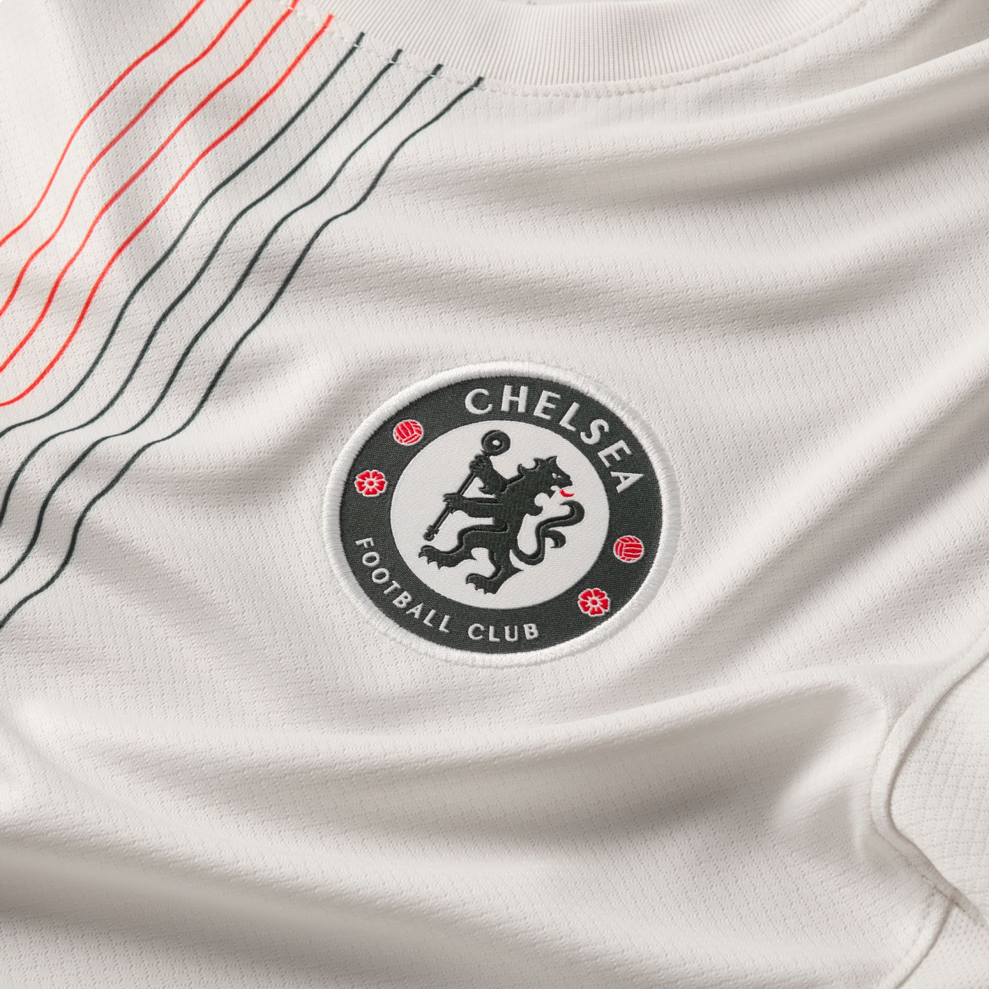 Close-up of a white Chelsea FC jersey featuring an embroidered club crest and diagonal red and black stripes on textured fabric.