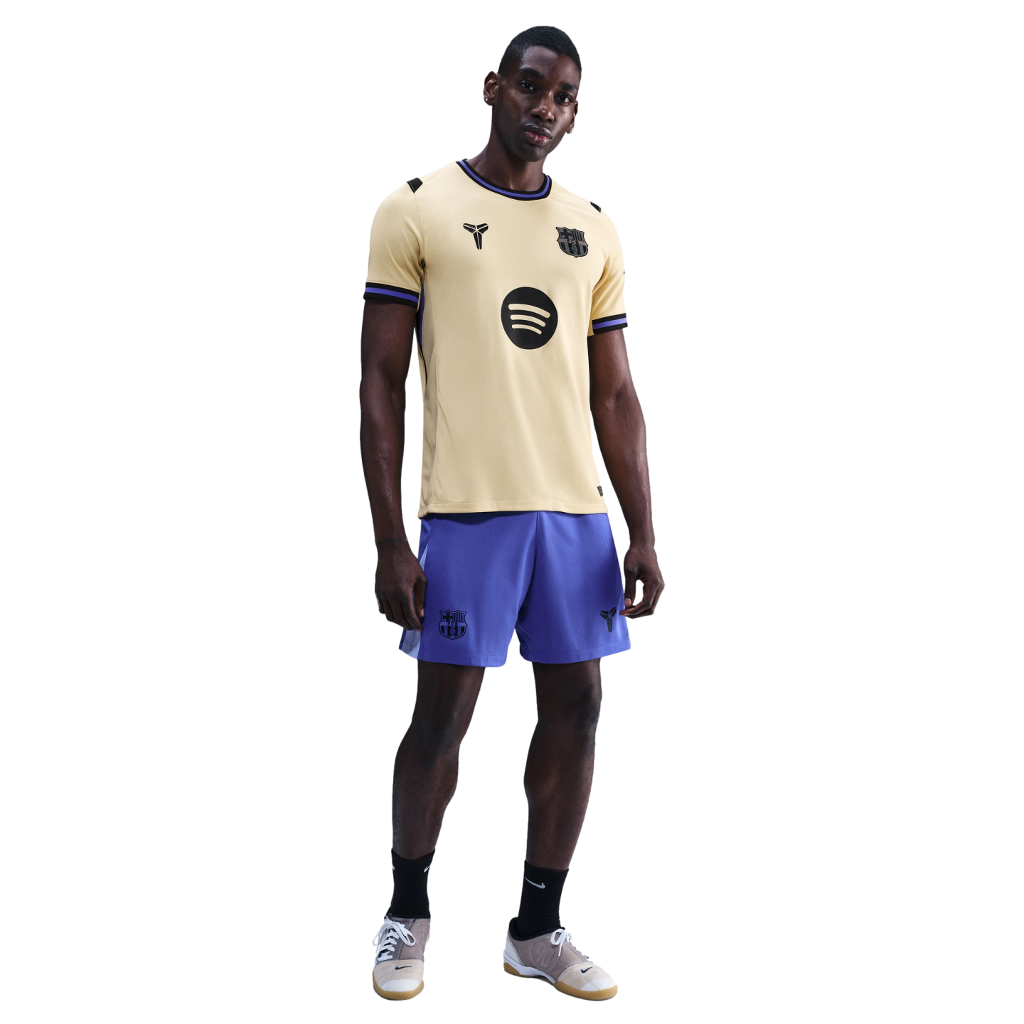 A man modeling a gold FC Barcelona x Kobe Bryant jersey with purple shorts and black socks against a black background.