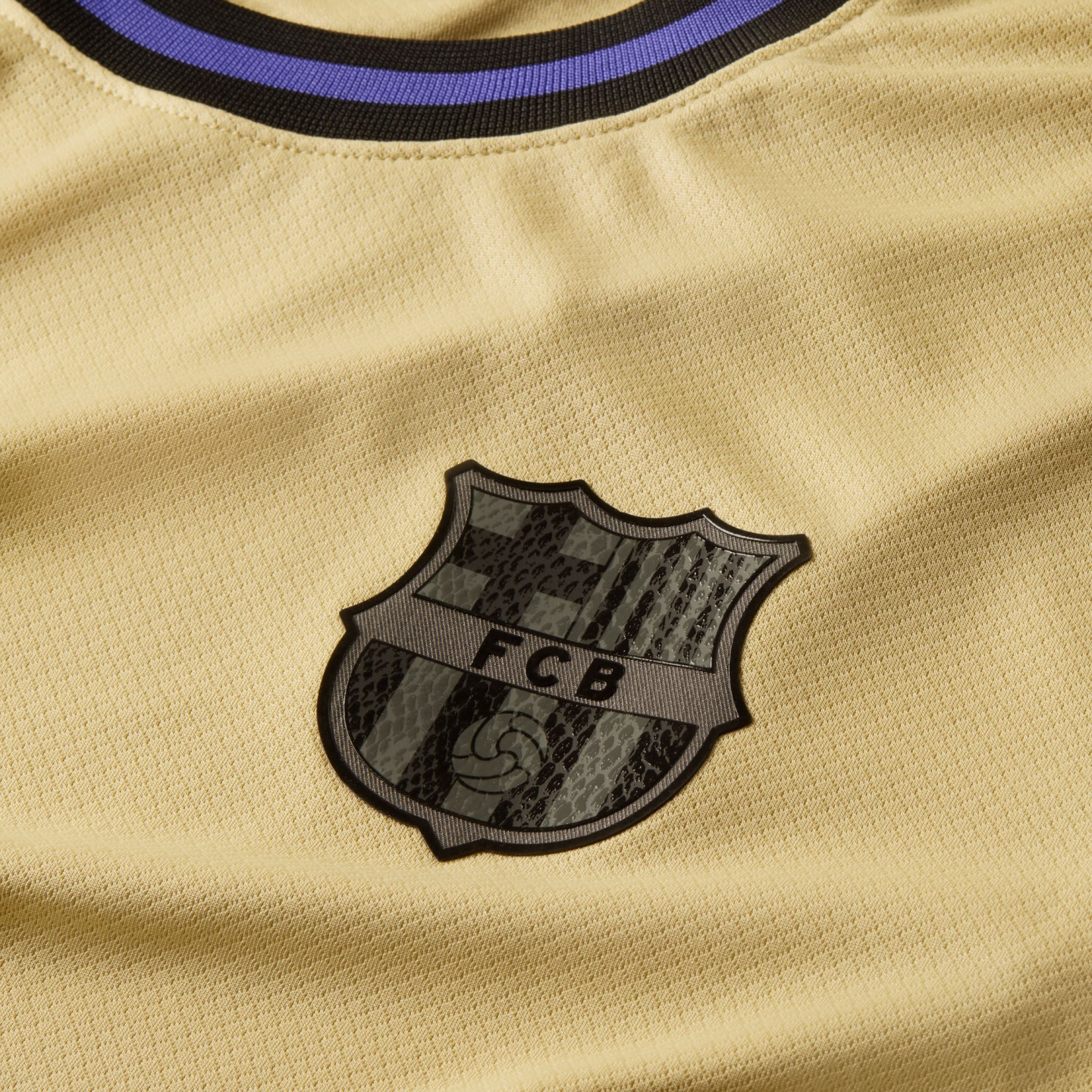 Close-up of a gold FC Barcelona soccer jersey featuring a monochrome black and grey club crest on the chest and a black collar with a blue stripe.