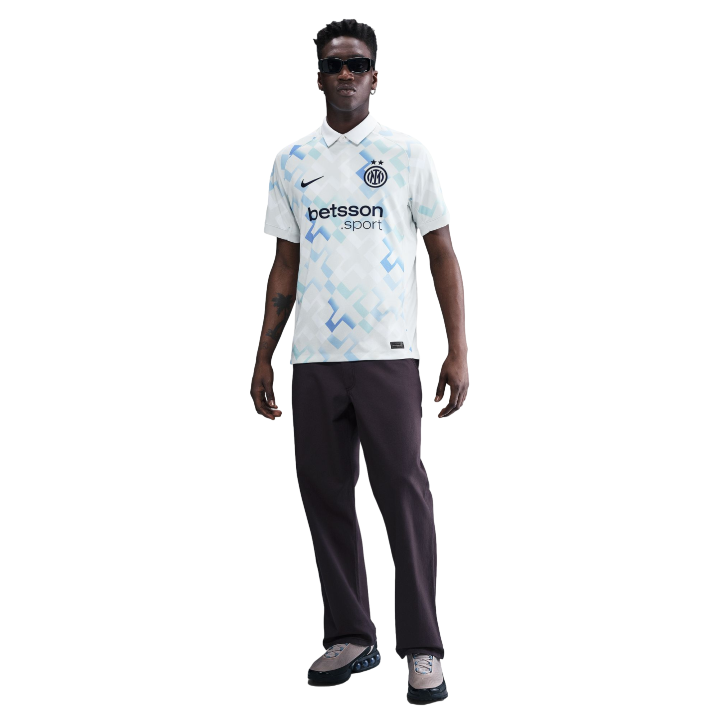 A man wearing a white and blue patterned Inter Milan soccer jersey, dark pants, and sunglasses, standing against a white background.