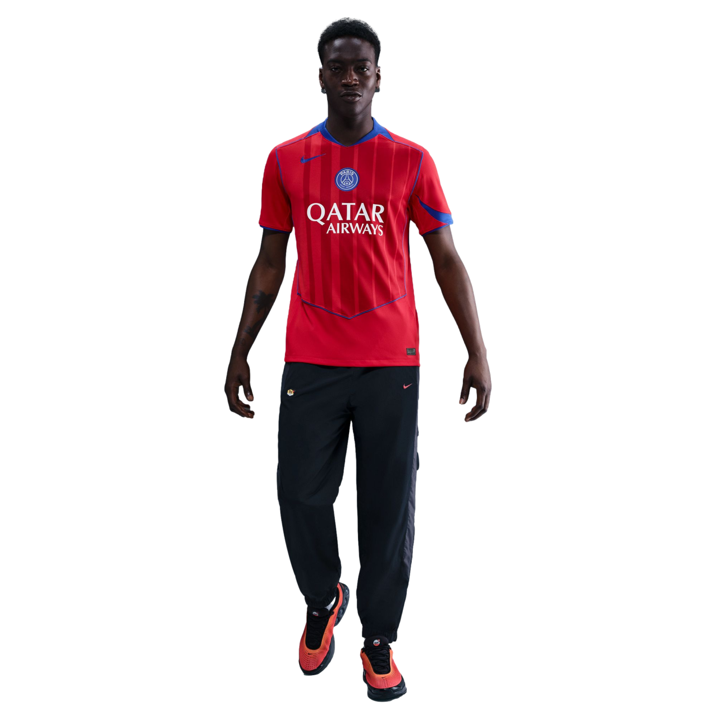 A man modeling a red Paris Saint-Germain soccer jersey, black track pants, and orange sneakers against a black background.