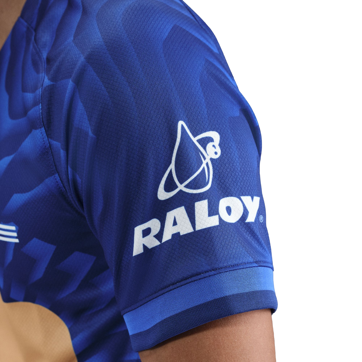 Close-up of a blue sports jersey sleeve featuring the white RALOY logo and graphic emblem against a patterned fabric.